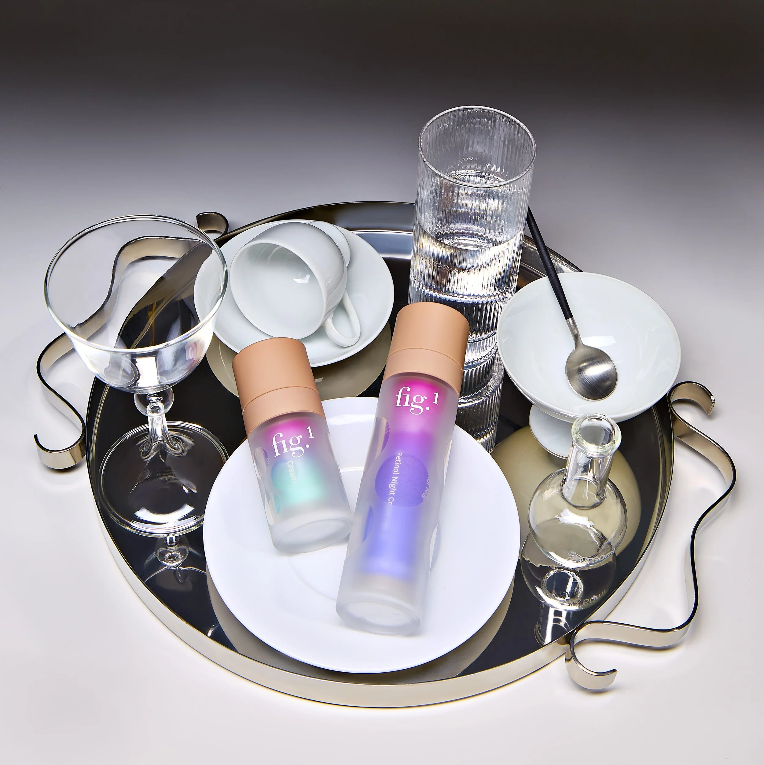 A collection of scattered glassware, including a tall, textured glass, wine glasses, and small bowls, placed on a reflective silver tray.