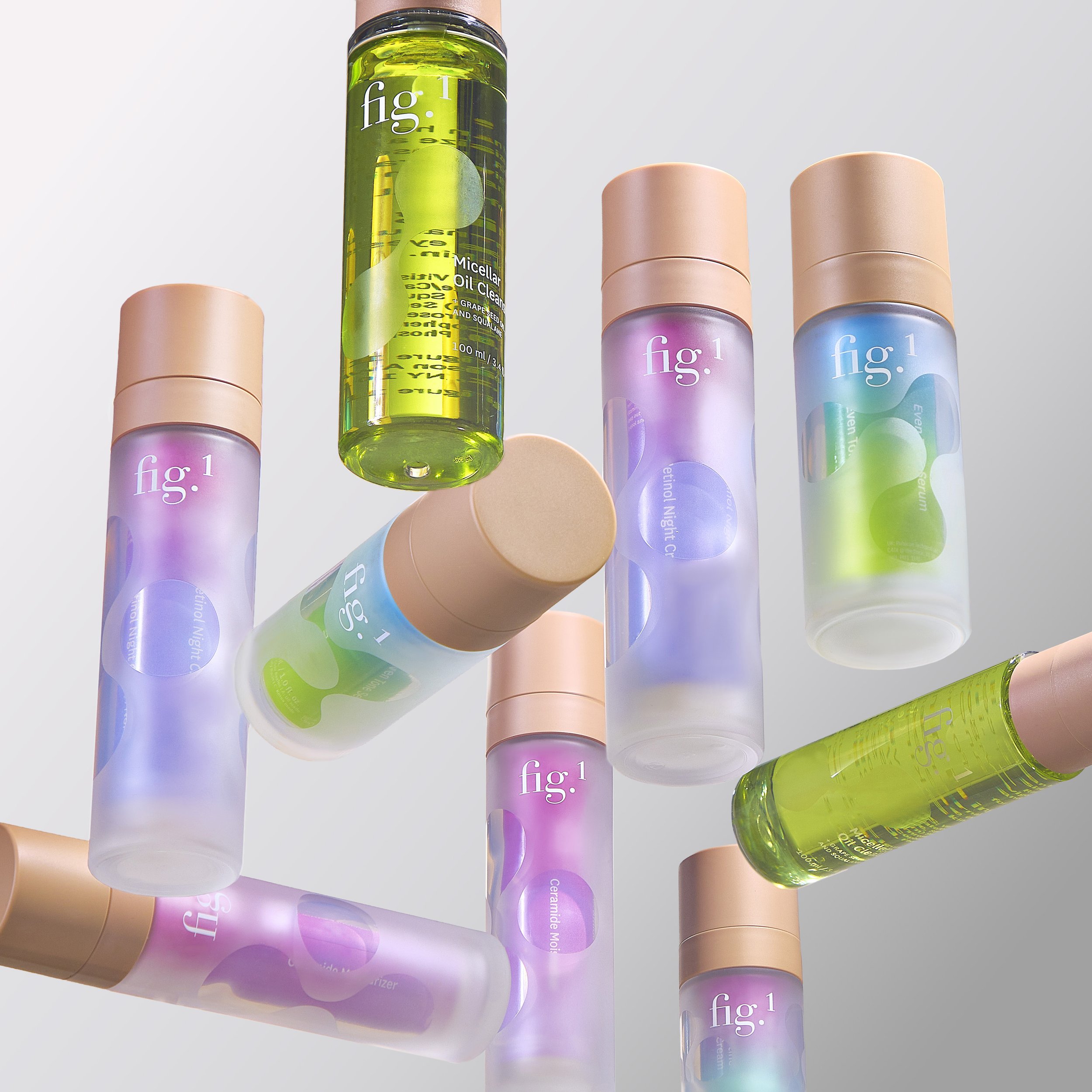 A collection of cosmetic spray bottles arranged on a white surface, including one green micellar oil cleanser and others with pastel-colored labels.