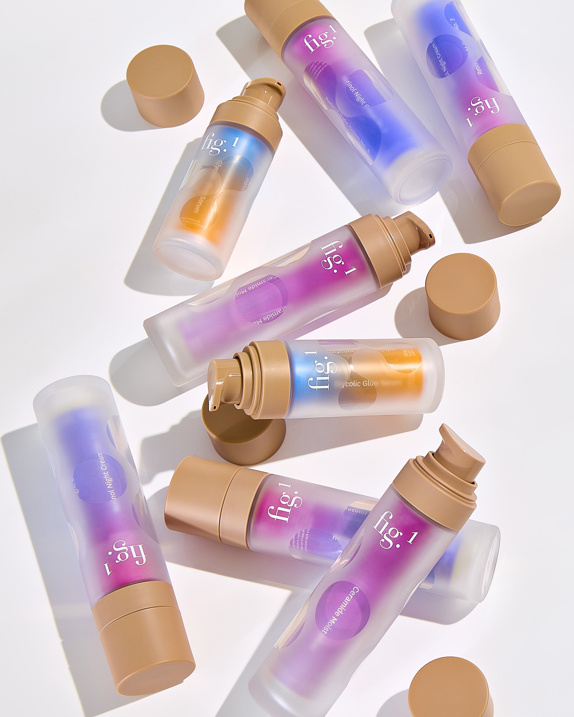 Multiple bottles of skincare products with beige caps and pastel-colored labels, placed on a white surface, casting shadows.