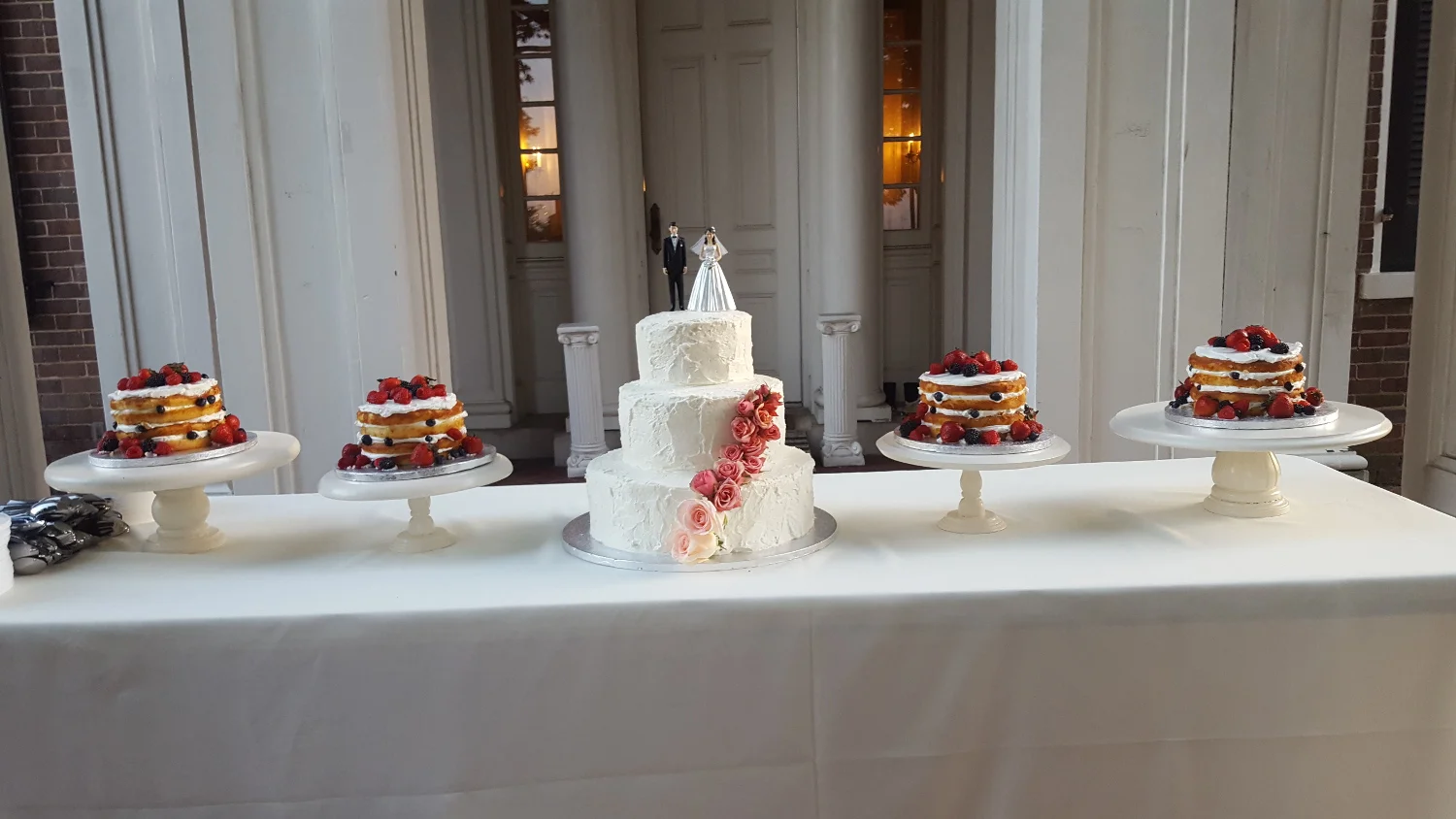 Cake display with 5 cakes. A 3 tier wedding cake with pink flowers and 4 naked cakes with fruit.