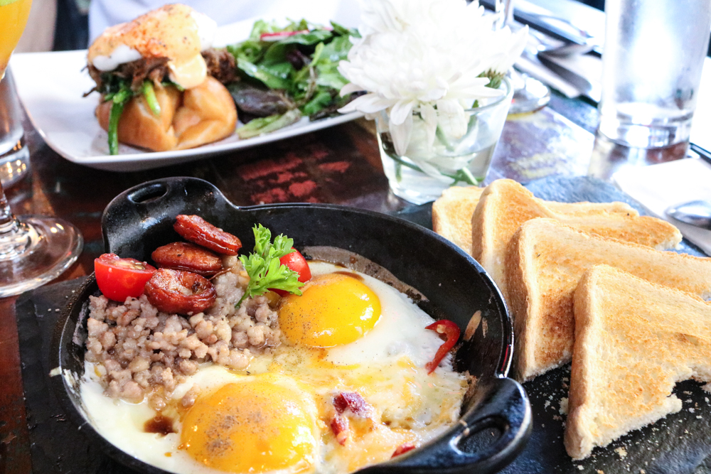 (front) Signature Bao, 2 eggs in skillet, chorizo, ground pork, tomatoes, pomme frites & soy sauce side with toasts (back) Sober Bao Benedict, braised & pulled pork shoulder with saute spinach served on fried "Bao" bun topped with a poached egg & spicy holl&aise sauce side salad