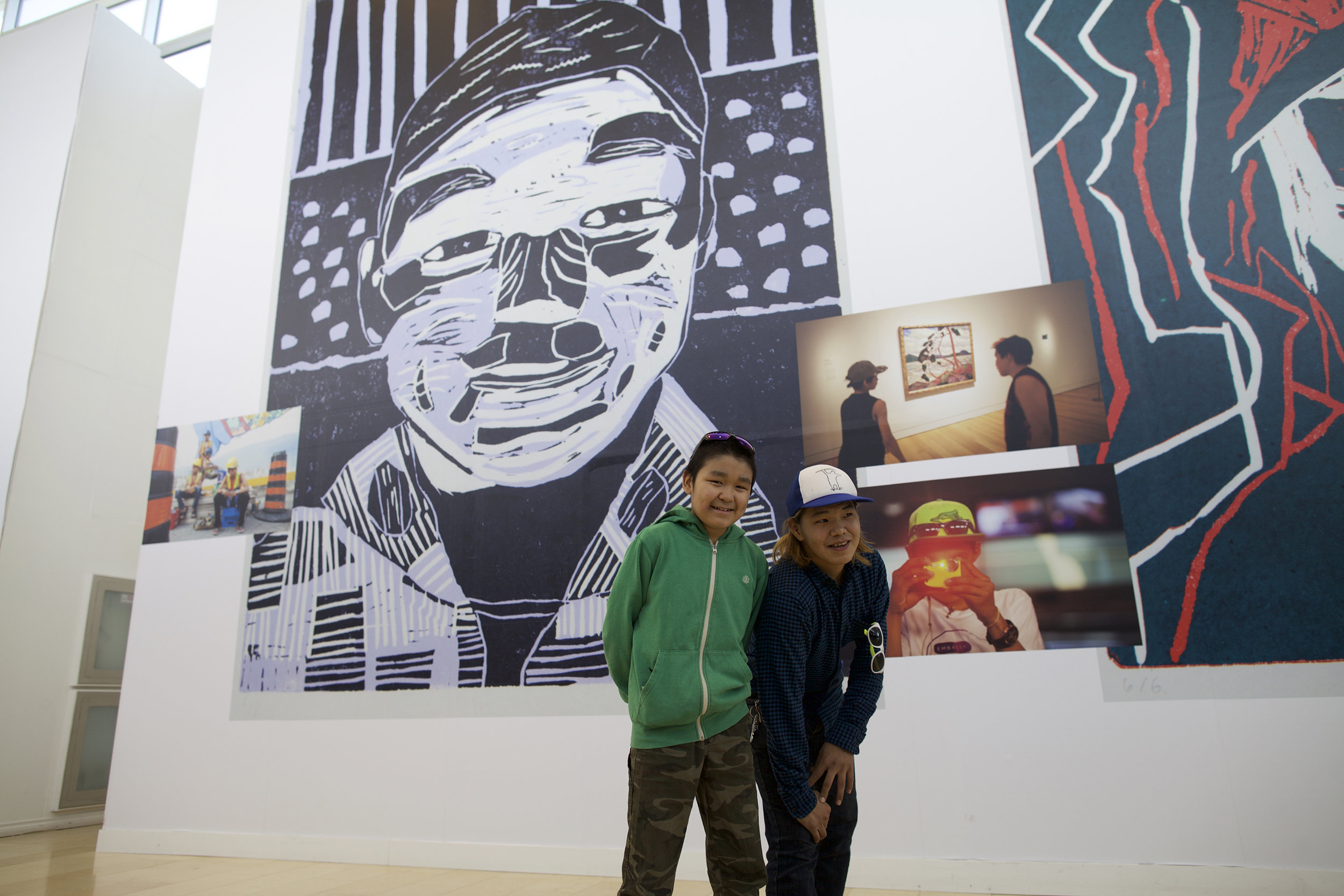 Tommy Quvianaqtuliaq, left, Parr Josephee, right. Tommy's self-portrait is the giant linocut image behind him, and Parr stands beside one of many photos of himself as part of the Piliriqatigiingniq mural project in Toronto, 2015.