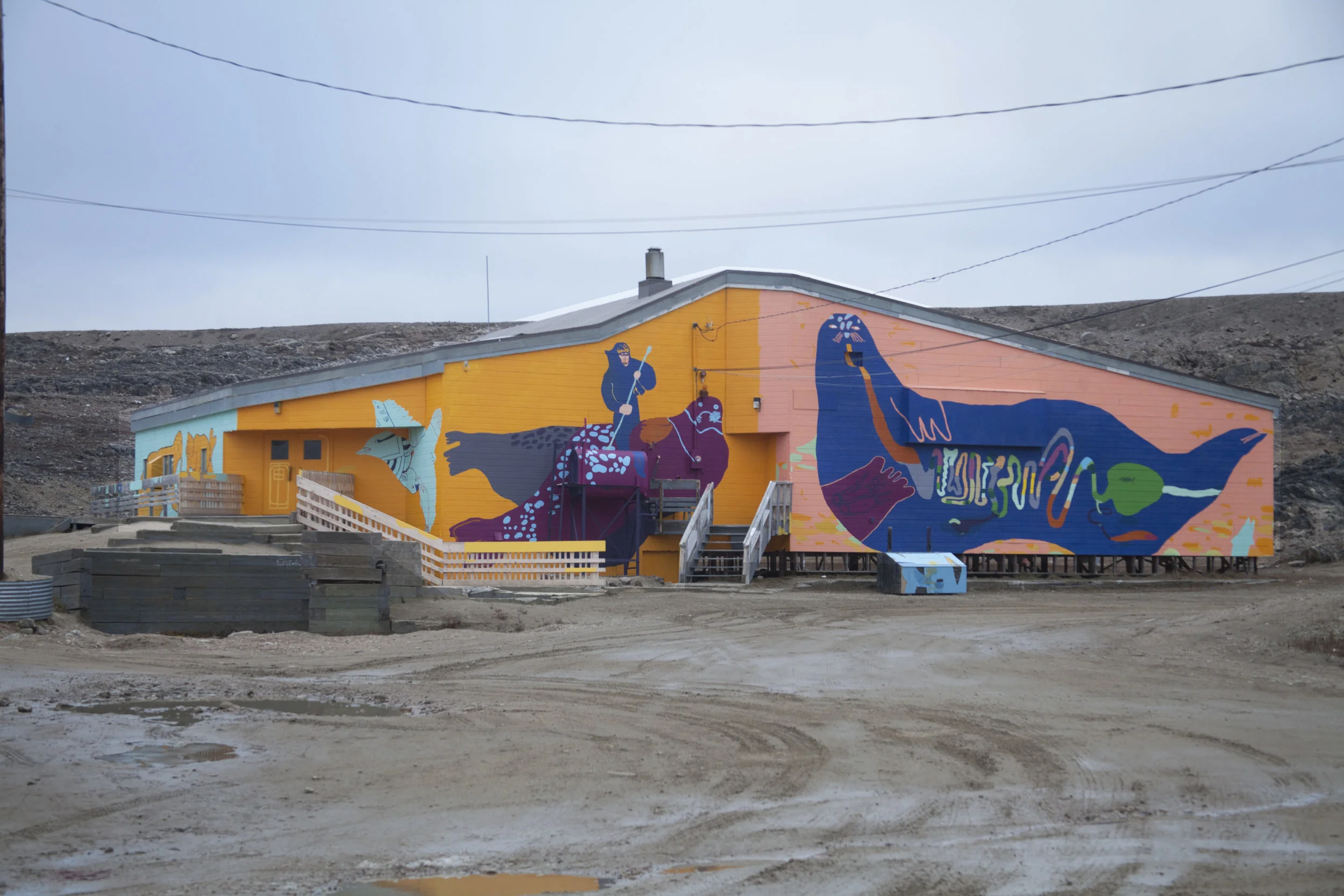 Front of the Community Hall. Left to right drawings by Ezeevalu Samayualie, Harry Josephee, Christine Adamie. Kevin Qimirpik, Tommy Quvianaqtuliaq, and Salomonie Ashoona. 