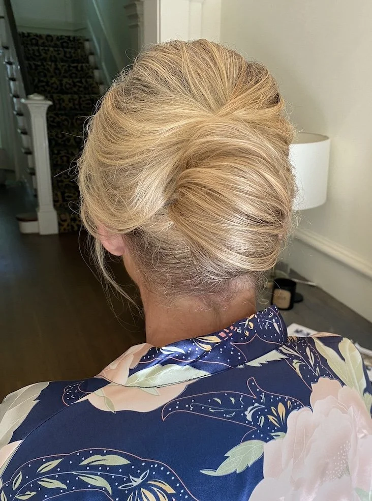 Back view of a woman with styled blonde hair and a blue floral robe, in a home interior setting.