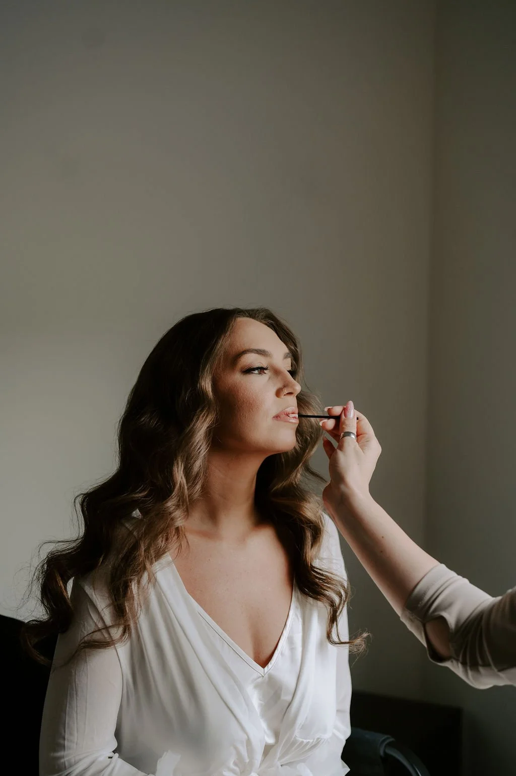 brunette bride with glam waves and tan skin sitting in the makeup chair