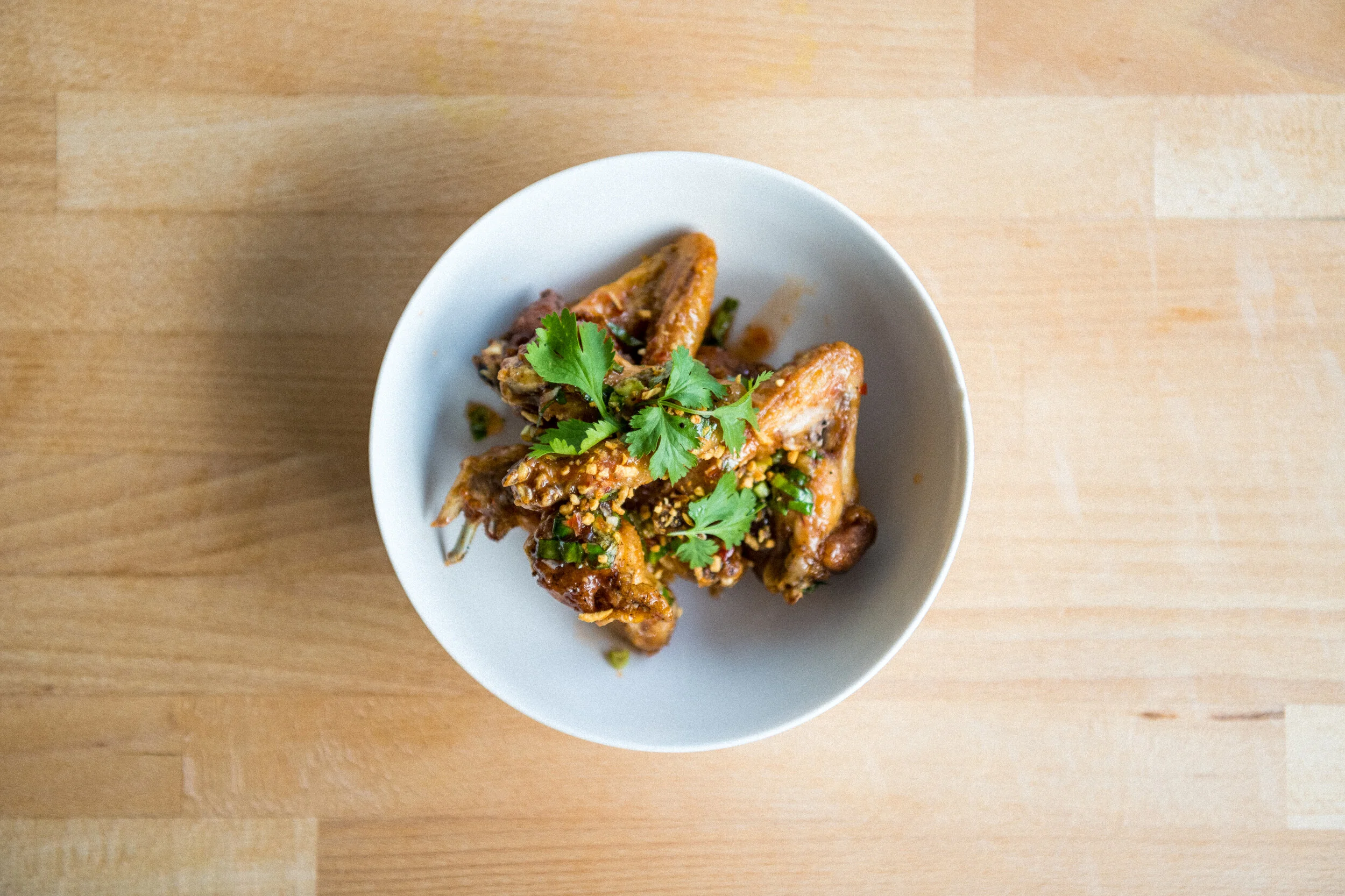   CHICKEN WINGS (GF) - 12    deep fried chicken wings marinated in fish sauce tossed with asian cilantro, cilantro, fried garlic, vinegar, black pepper, lime juice    (LARG SIZE+8)   