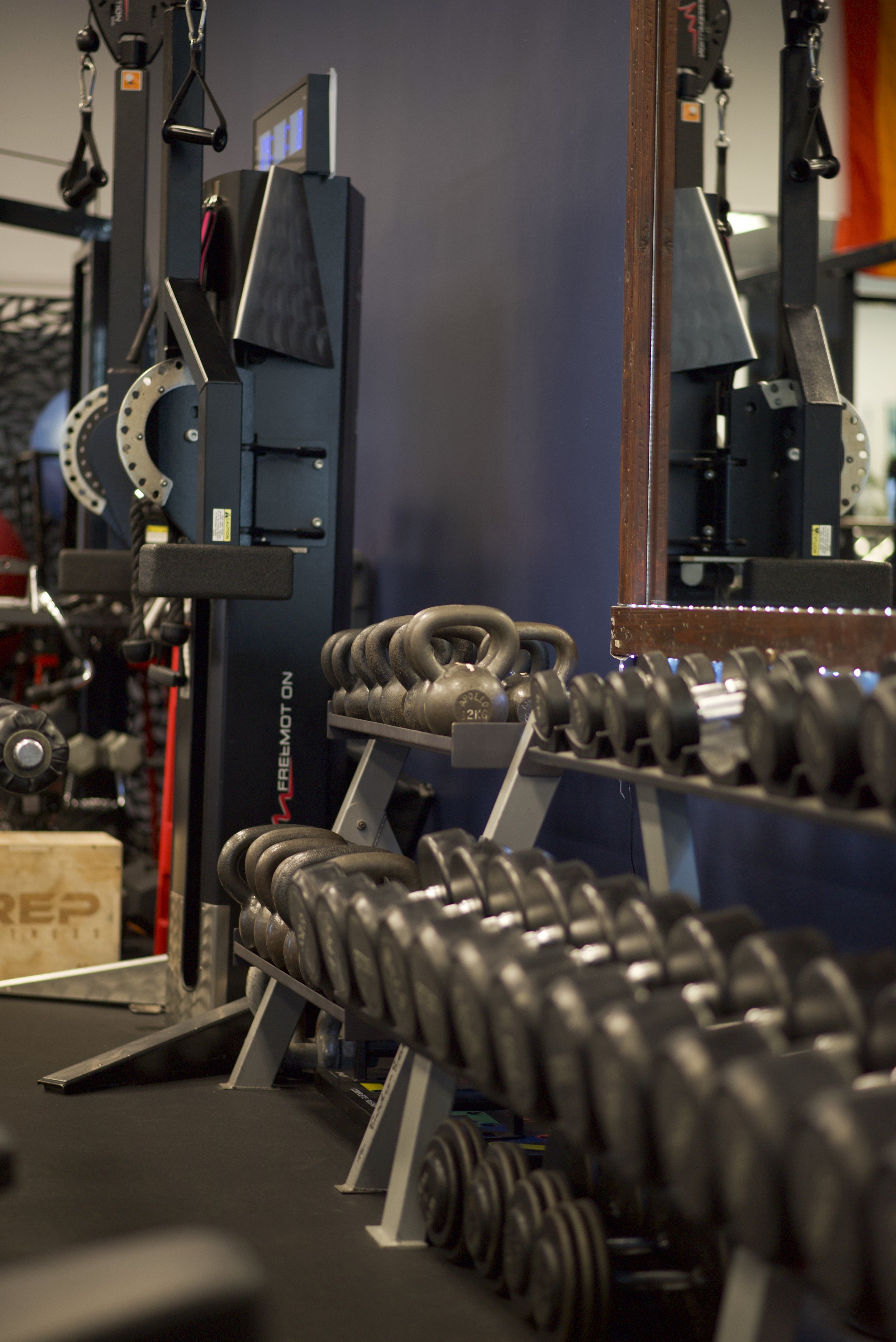A gym with a rack of black dumbbells, a mirror, and weightlifting equipment against dark and wooden walls.