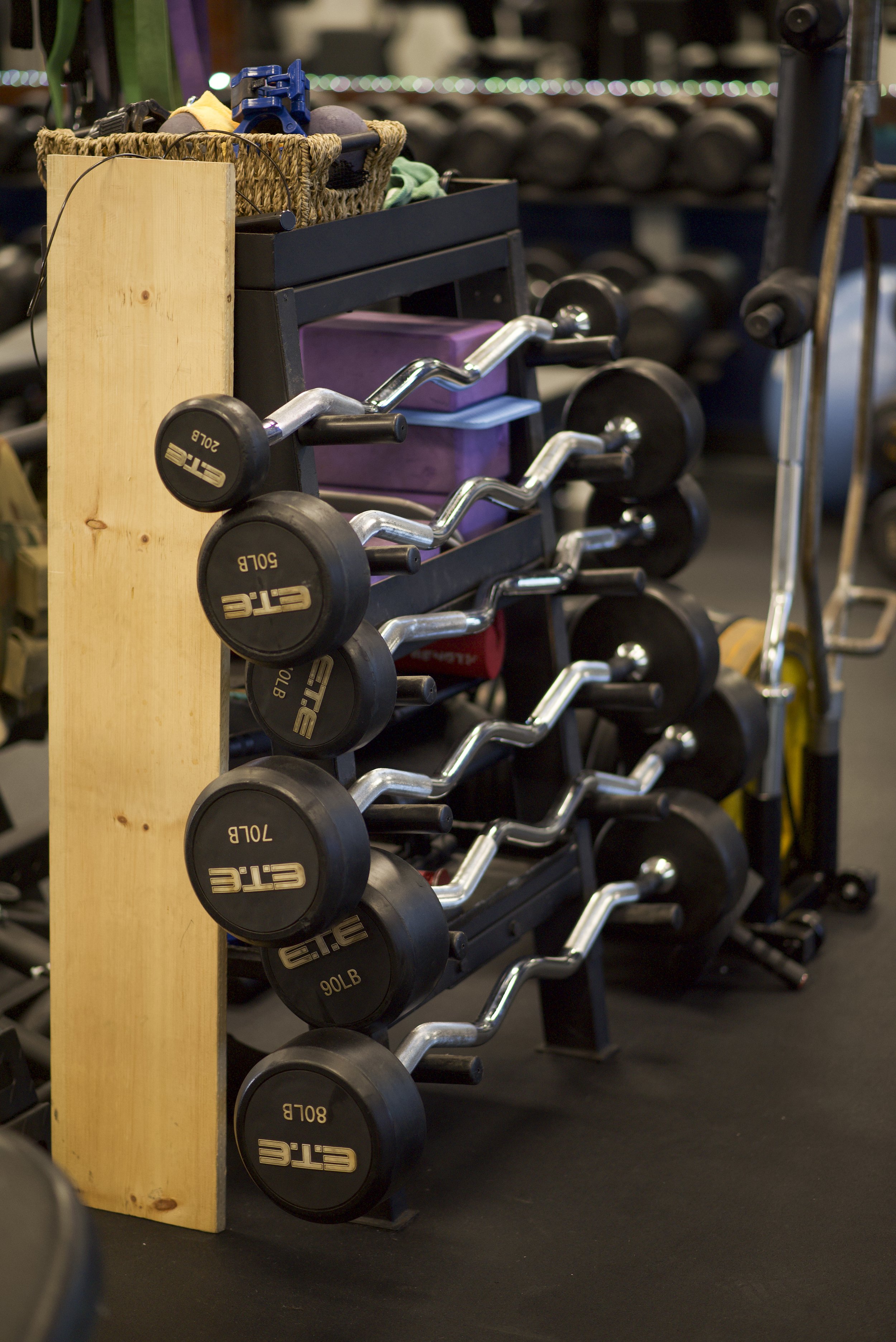 A rack of seven chrome-bent dumbbells with black weight plates labeled 5, 10, 15, 20, 25, 30, and 40 pounds, arranged in ascending order from bottom to top, in a gym environment.