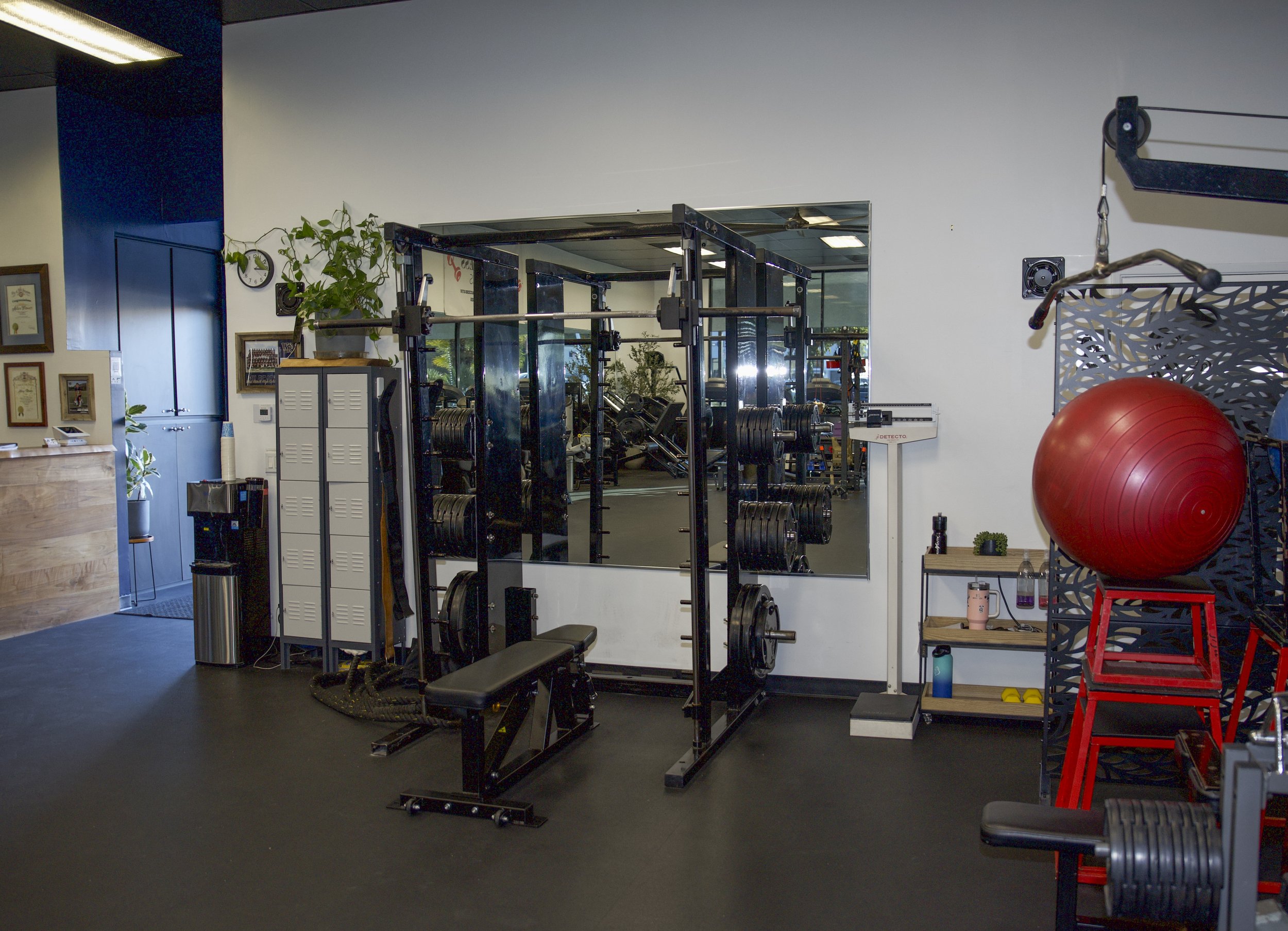 Fitness gym with weightlifting equipment, a red exercise ball, and a mirror on the wall.