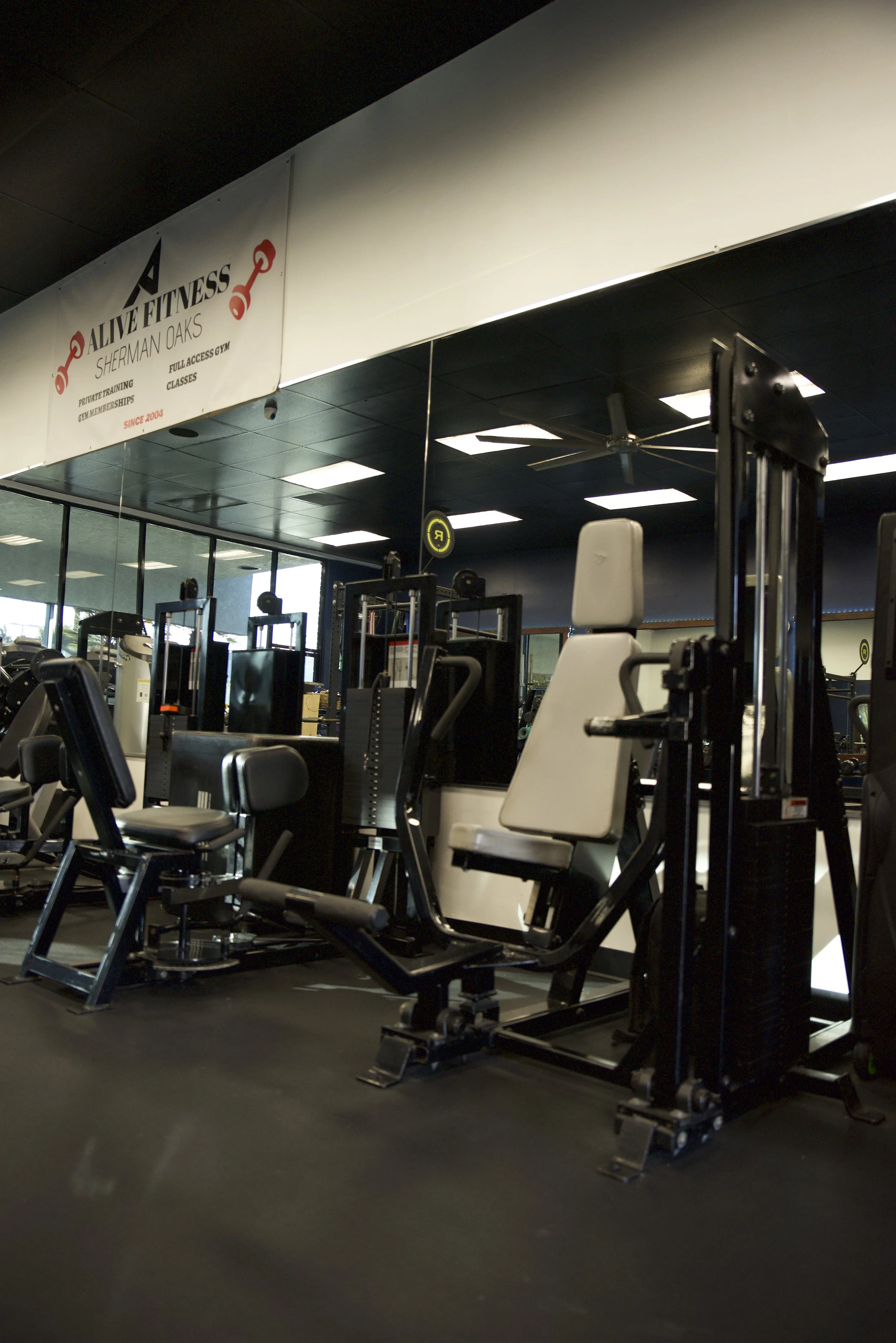 Inside a gym with various exercise machines and a sign that reads 'Alive Fitness Sherman Oaks'.