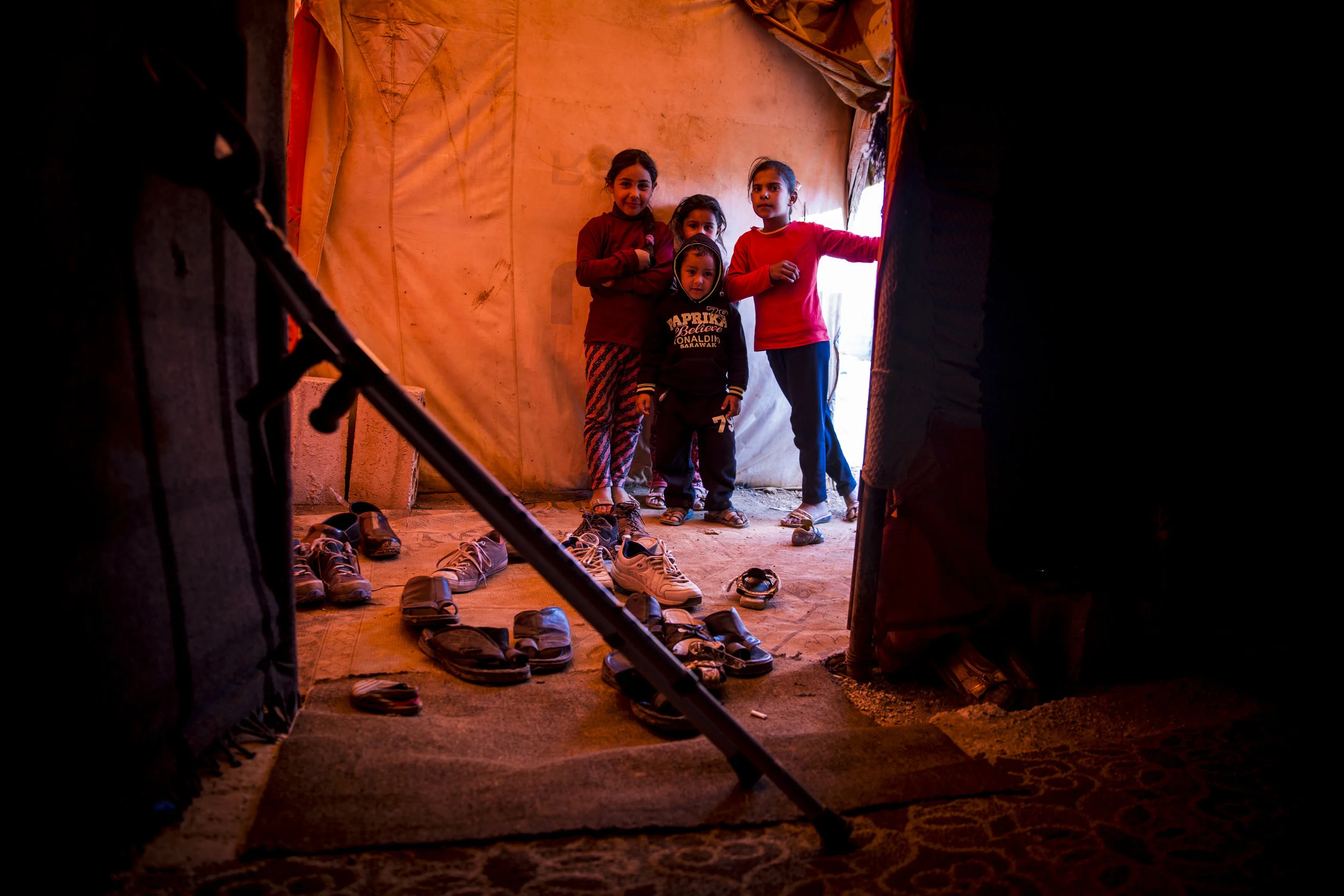 Amira, Sara, Riham, and Halid peer into the tent where 13 members of two families share the small space. Both families fled Syria in 2013 when shellings and bombs began to fall near their homes. 04.21.2016
