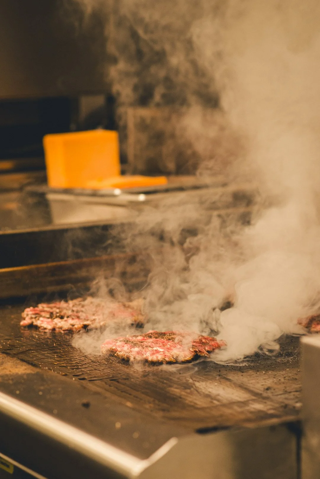 Burger-Patties brutzeln auf dem Grill, umgeben von aufsteigendem Rauch