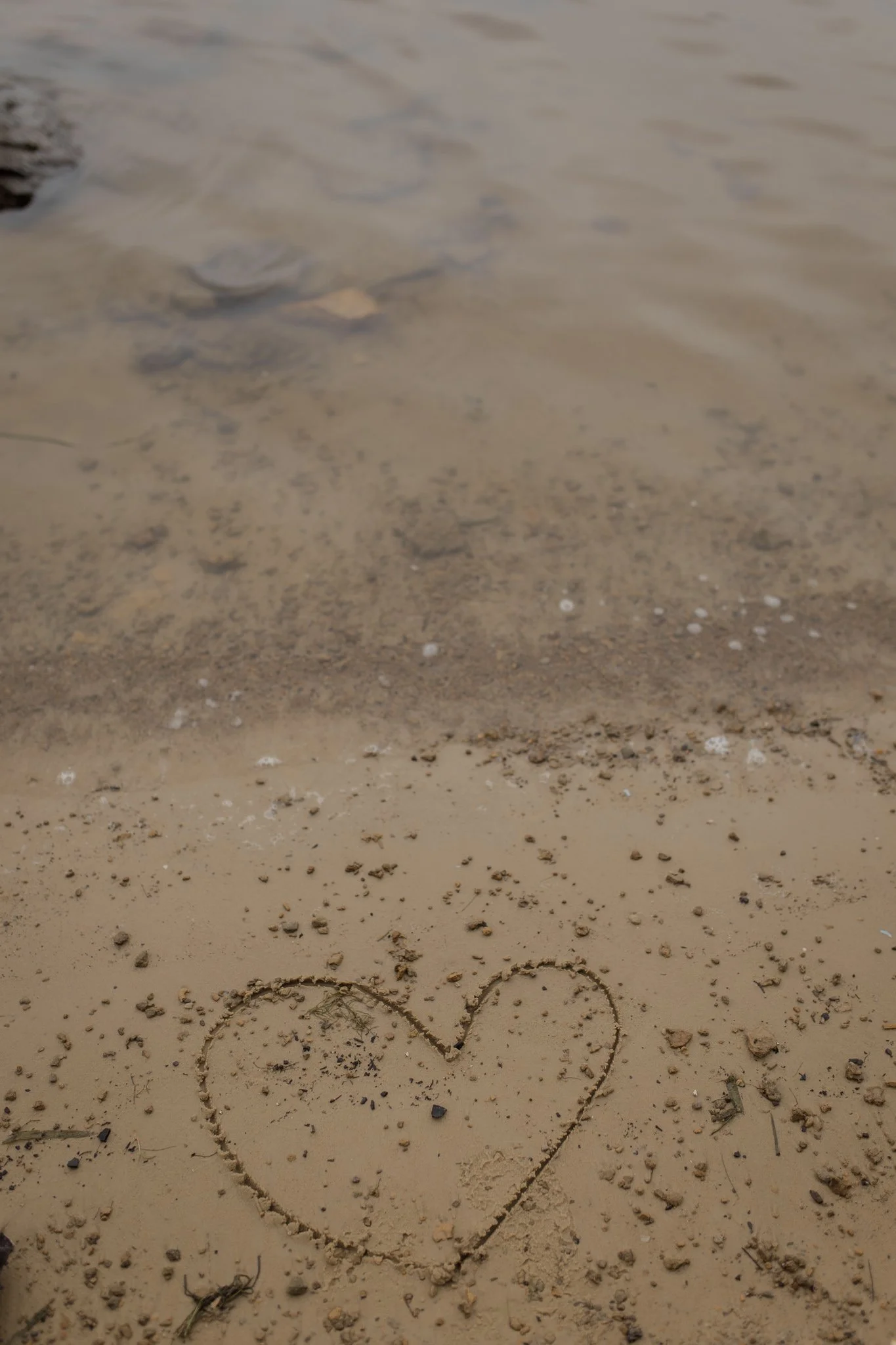 A heart shape drawn with a stick in the sand on a beach, surrounded by small pebbles and shells showing God's love for us.