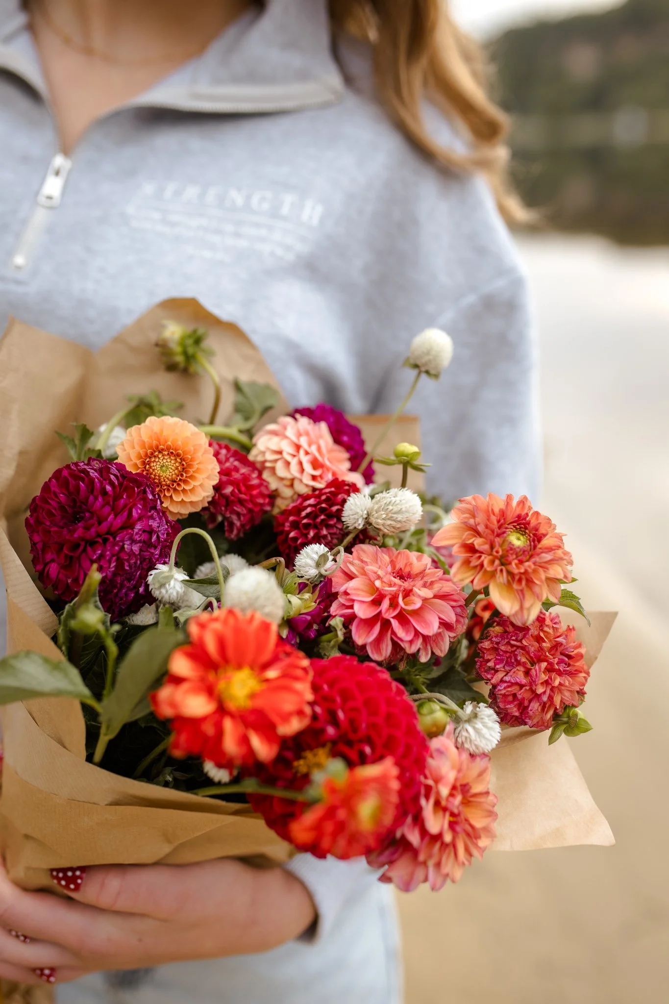 A person holding a bouquet of colorful flowers wrapped in brown paper.
