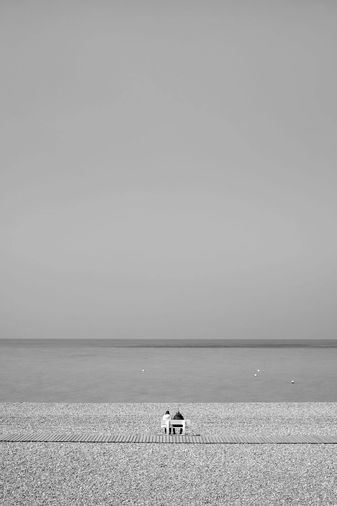  Black-and-white seaside photograph on the beach at Le Tréport, Normandy, couple seated enjoying the sea view, by Chris Perona. 