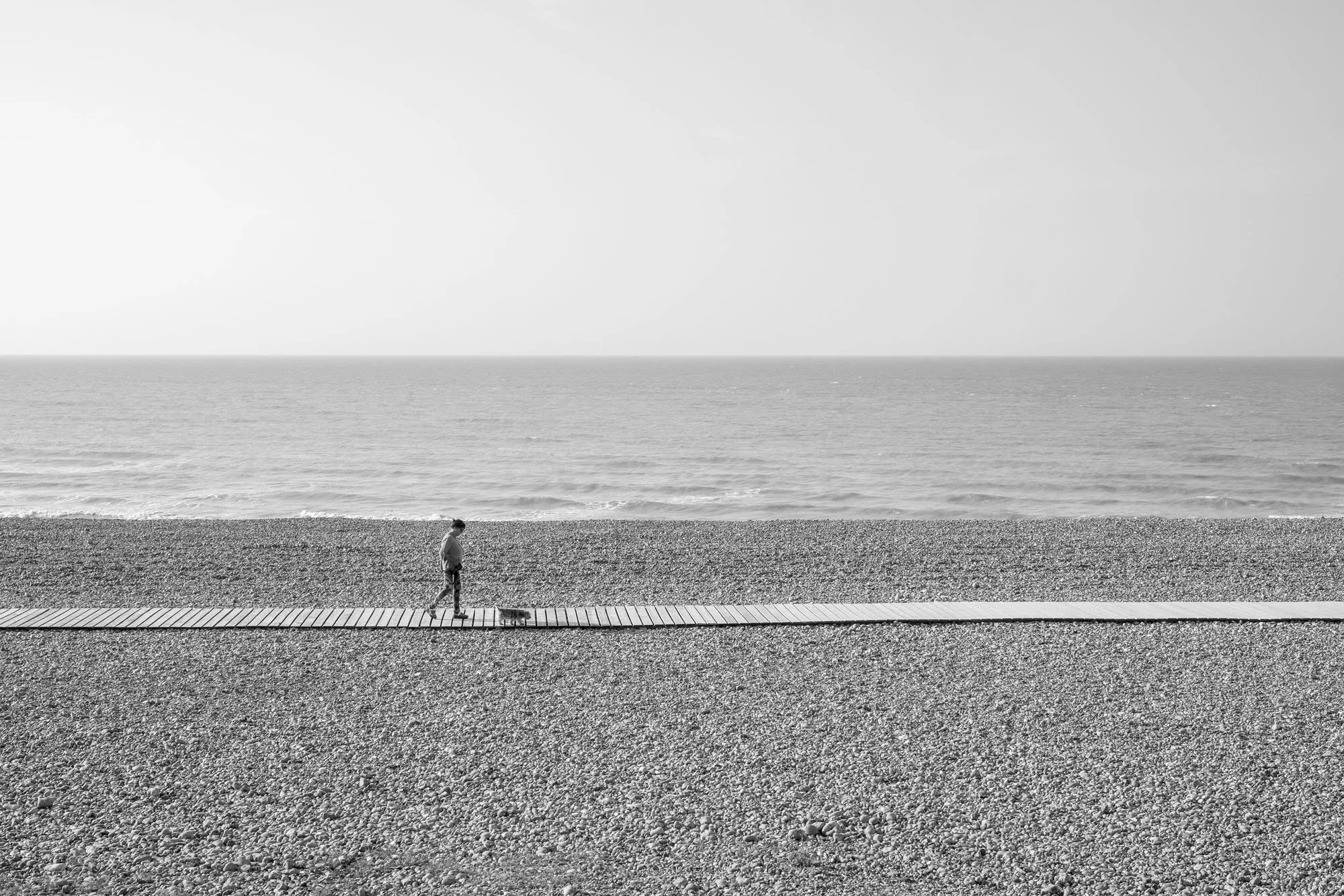  Black-and-white seaside photograph on the beach at Le Tréport, walking man with his dog, Normandy, by Chris Perona. 