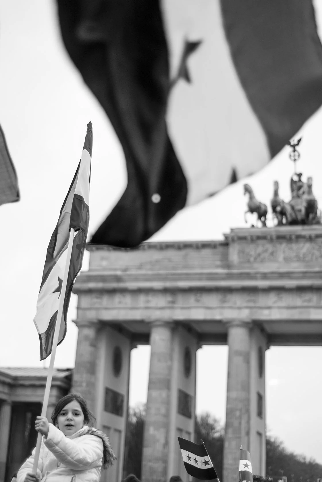  Girl waving a flag in front of the Brandenburg Gate during a demonstration, Berlin. Candid street portrait by Chris Perona. 