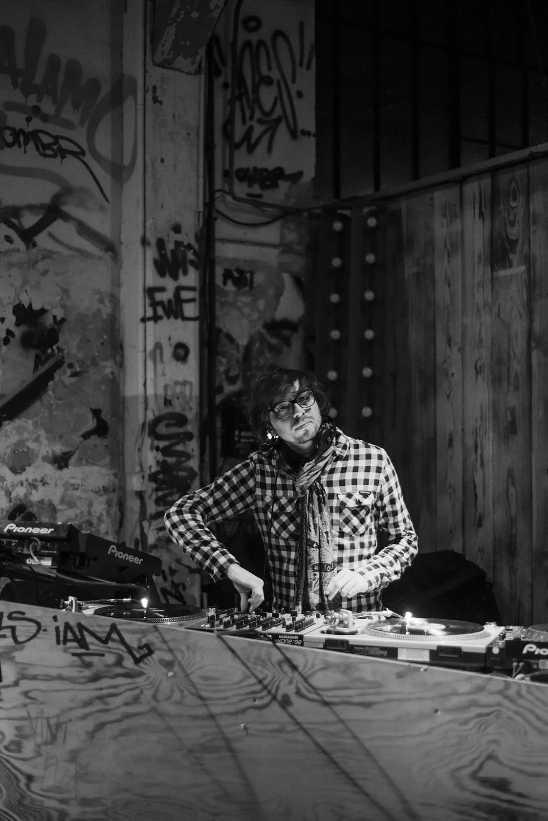  DJ in a checked shirt at the turntables in a graffiti-covered club, Berlin. Candid portrait by Chris Perona. 