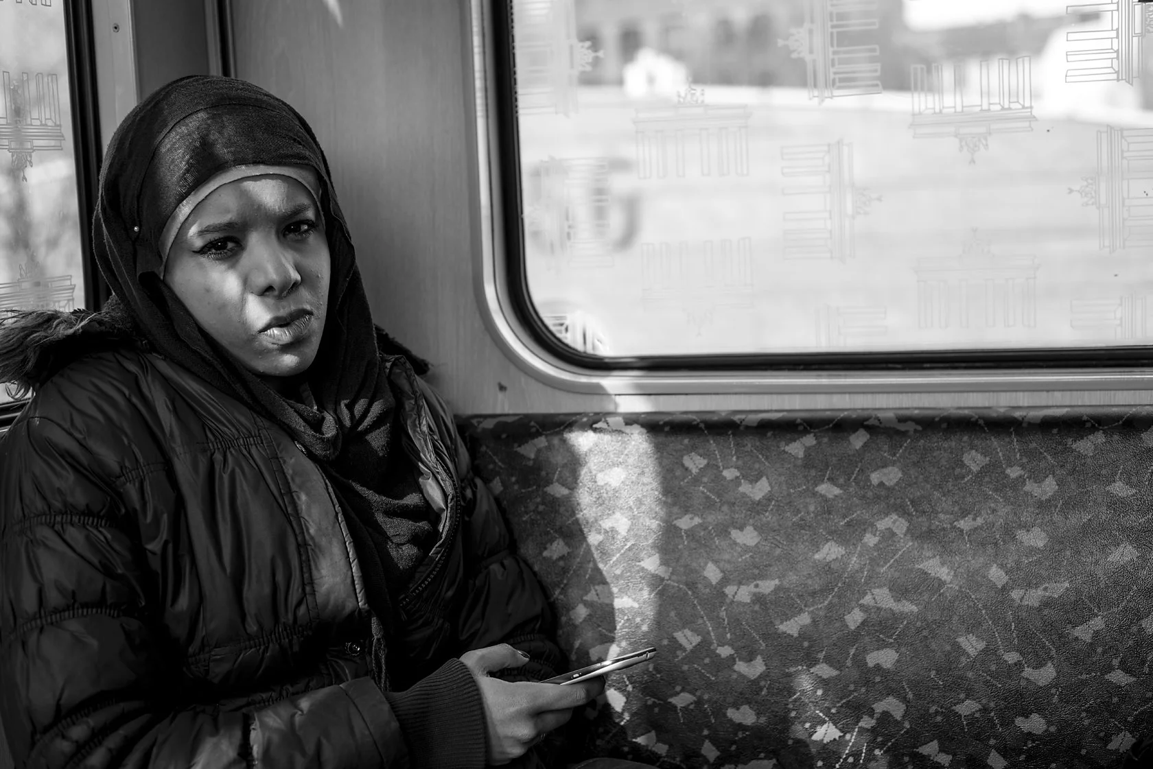  Young woman in a dark headscarf and puffer jacket on a Berlin S-Bahn, looking at the camera. Candid street portrait by Chris Perona. 