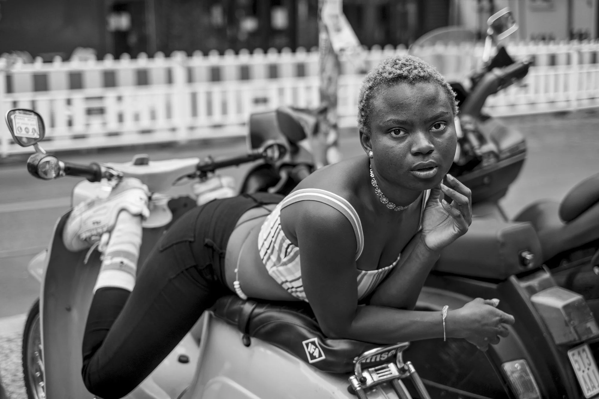  Young woman with short bleached hair lying across a parked scooter, Berlin. Candid street portrait by Chris Perona. 