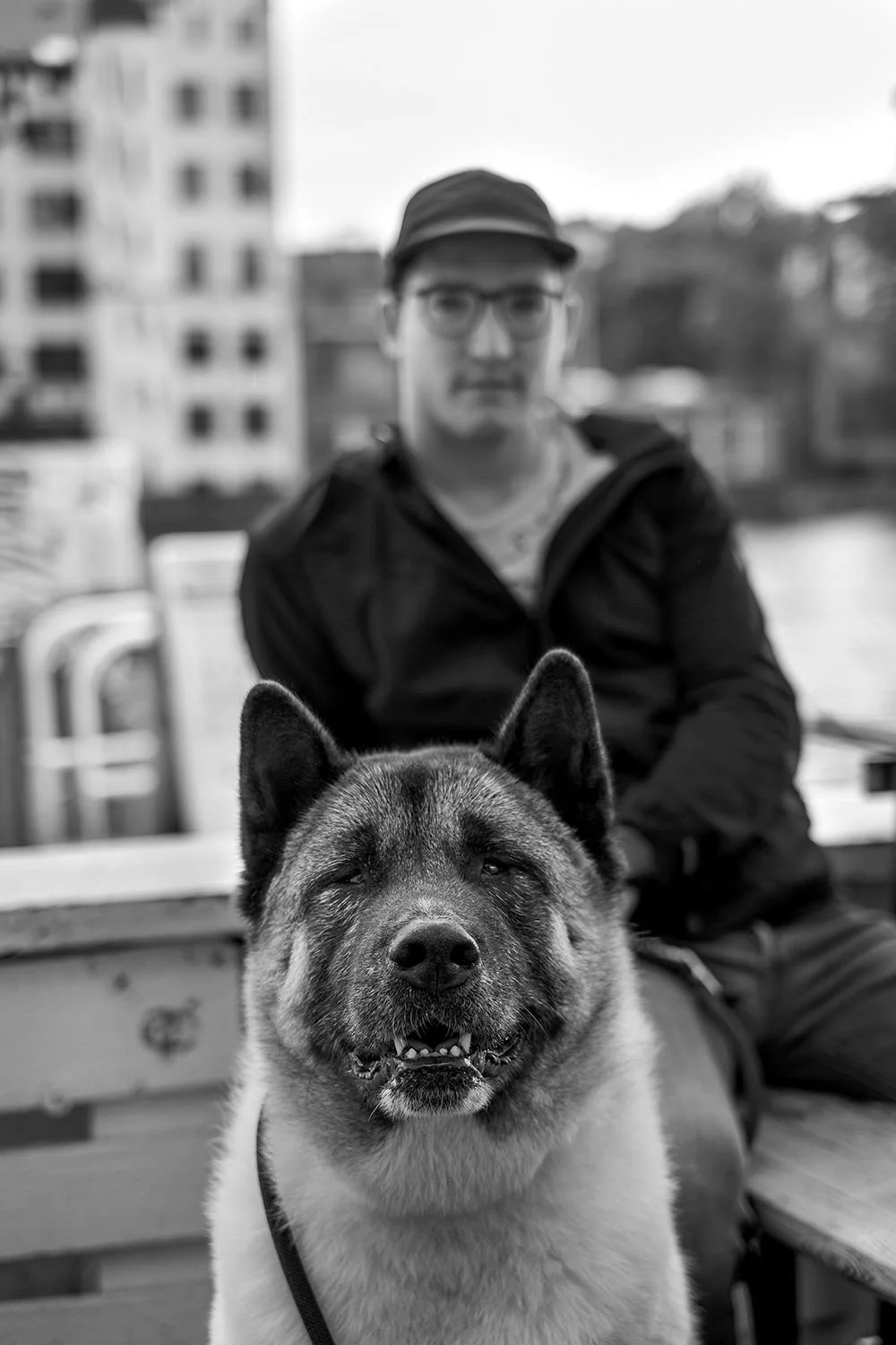  Young man in a cap and glasses by the river, his large dog in the foreground, Berlin. Candid street portrait by Chris Perona. 