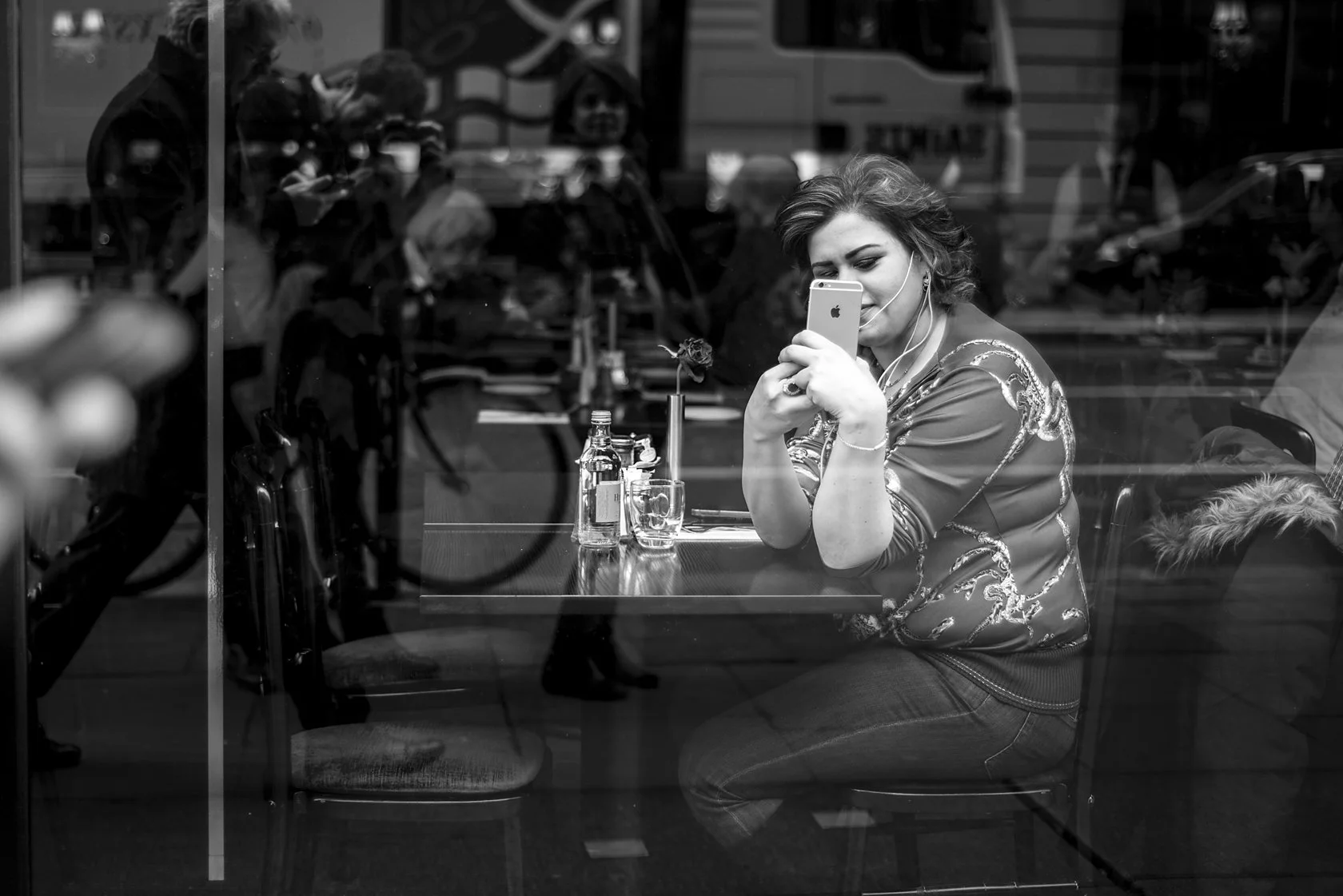 Woman in a patterned top seated behind a café window, hand to her face, London. Candid street portrait by Chris Perona. 