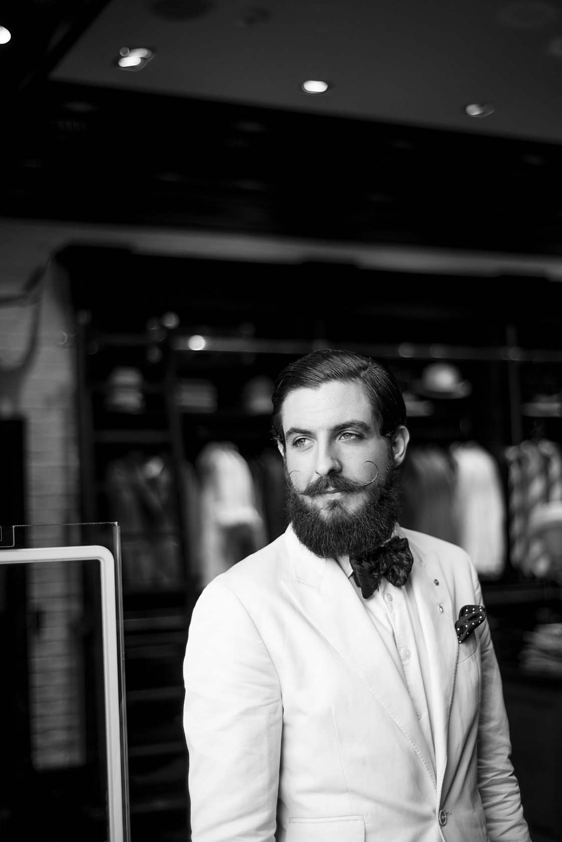  Bearded man in a white jacket standing in a shop doorway, London. Candid street portrait by Chris Perona. 