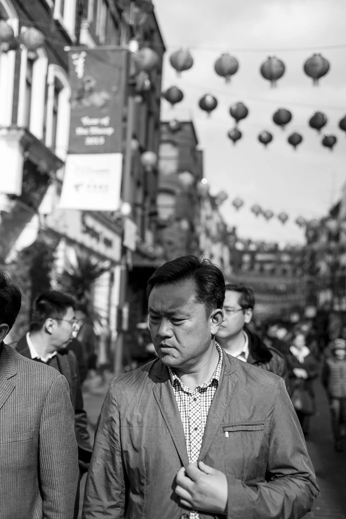  Man walking through Chinatown beneath hanging lanterns, London. Candid street portrait by Chris Perona. 
