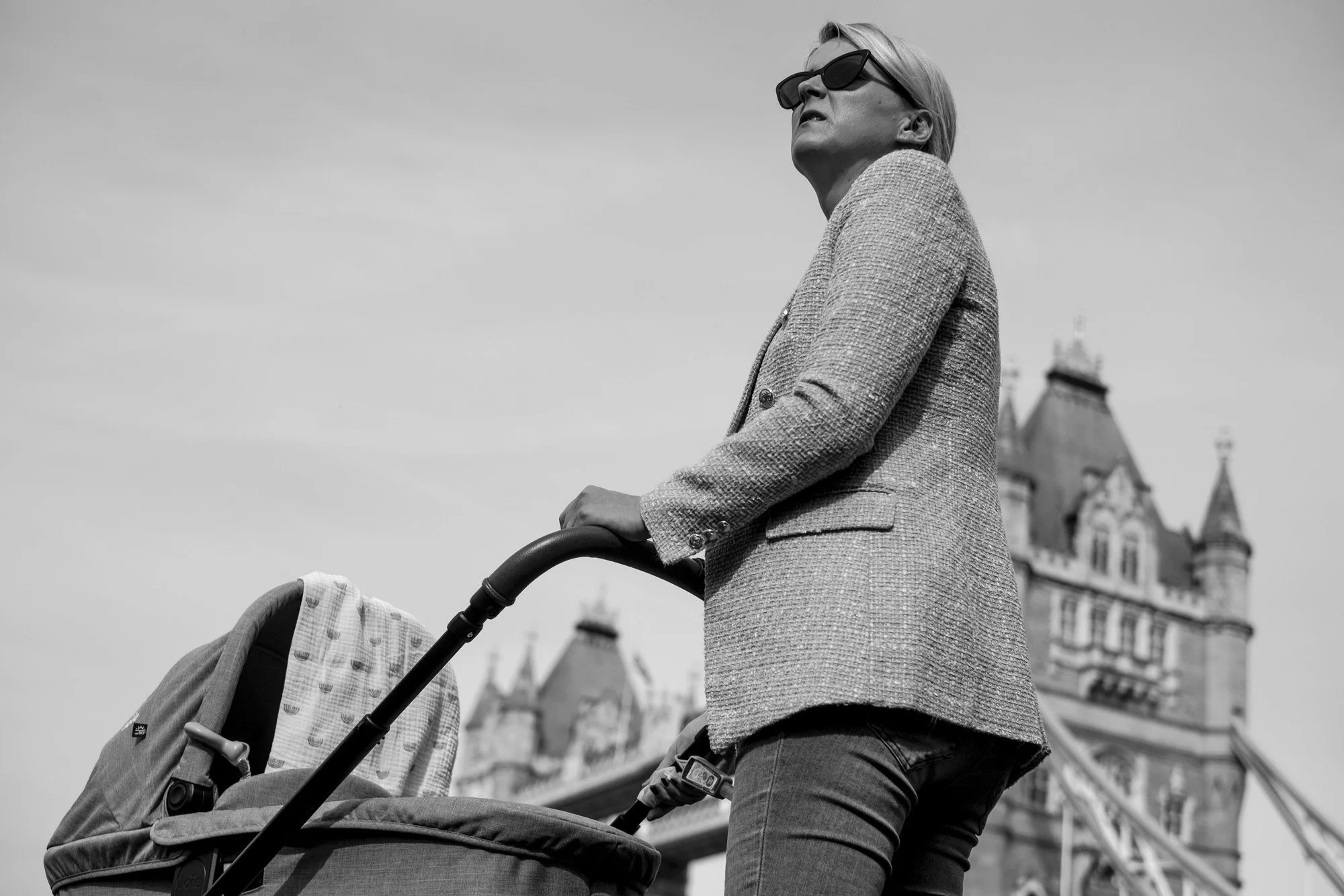  Woman in sunglasses and a tweed jacket pushing a pram near Tower Bridge, London. Candid street portrait by Chris Perona. 