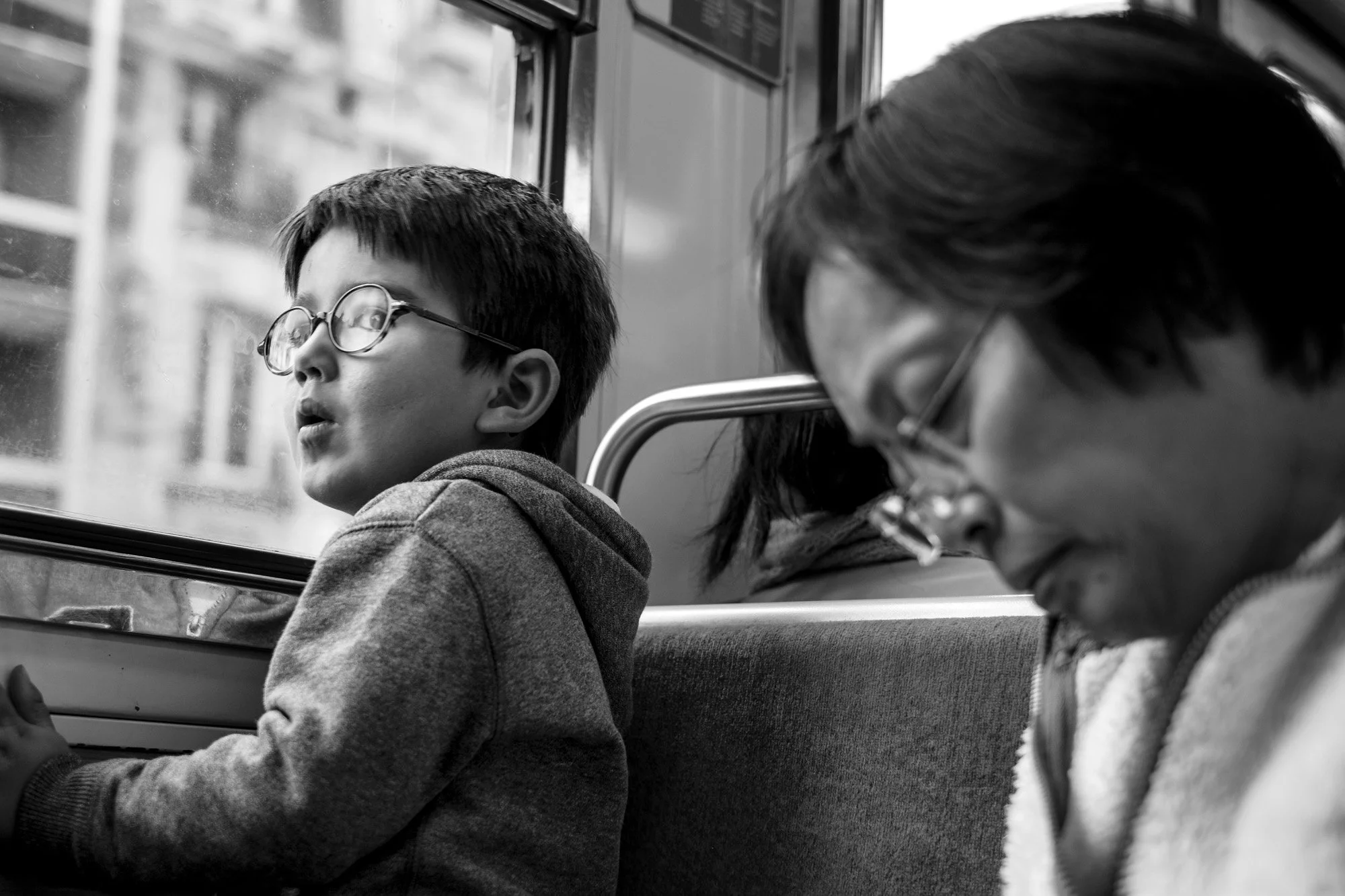  Boy with glasses looking out on a bus beside a dozing woman, Paris. Candid street portrait by Chris Perona. 