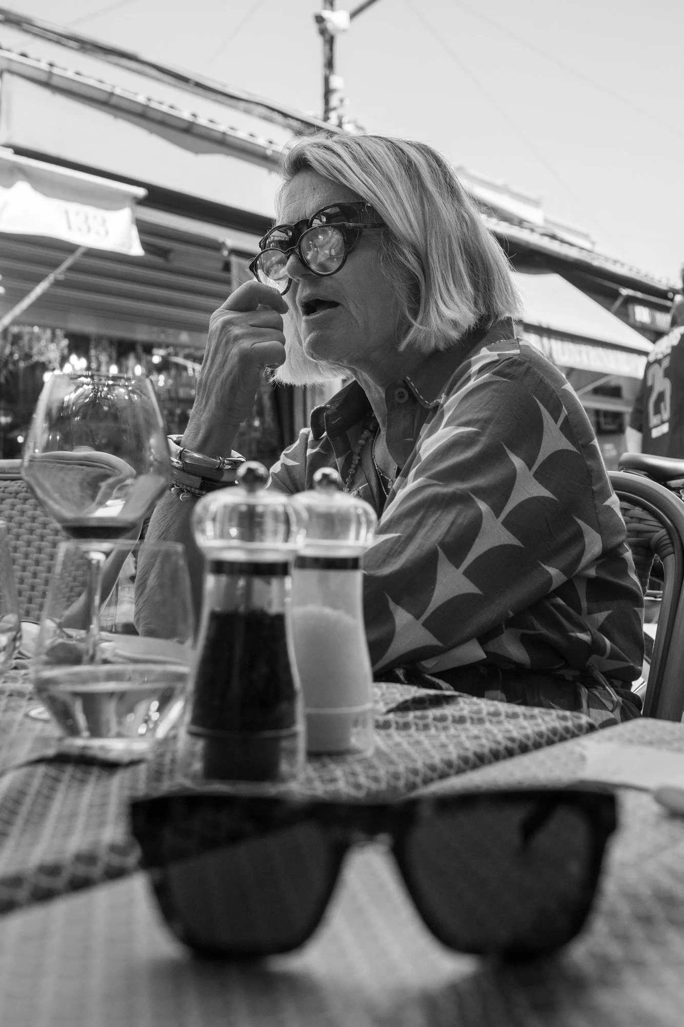  Woman in sunglasses and a star-print top at a café terrace, Paris. Candid street portrait by Chris Perona. 