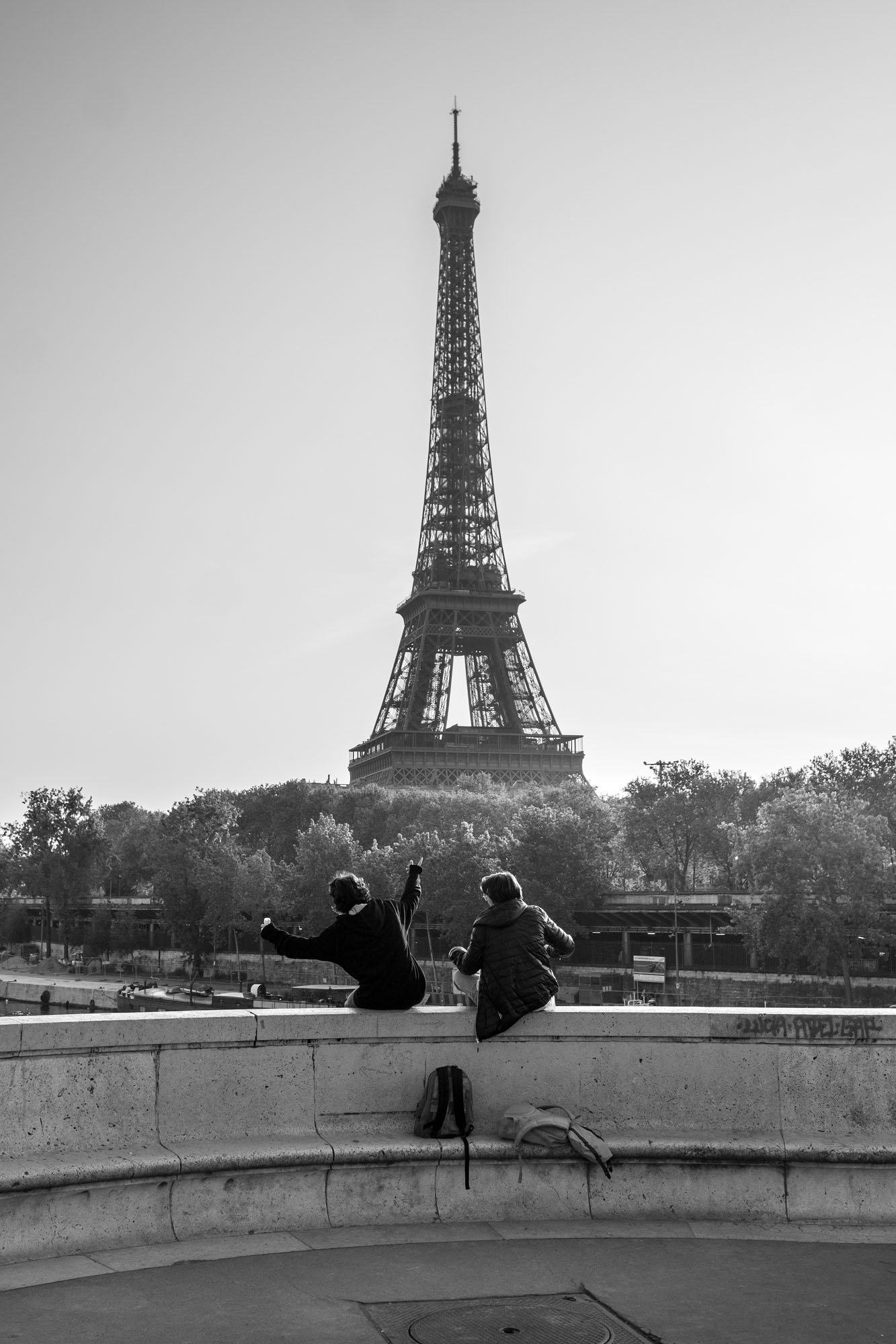  Two people sitting on the parapet facing the Eiffel Tower, Pont de Bir-Hakeim, Paris. Street photograph by Chris Perona. 