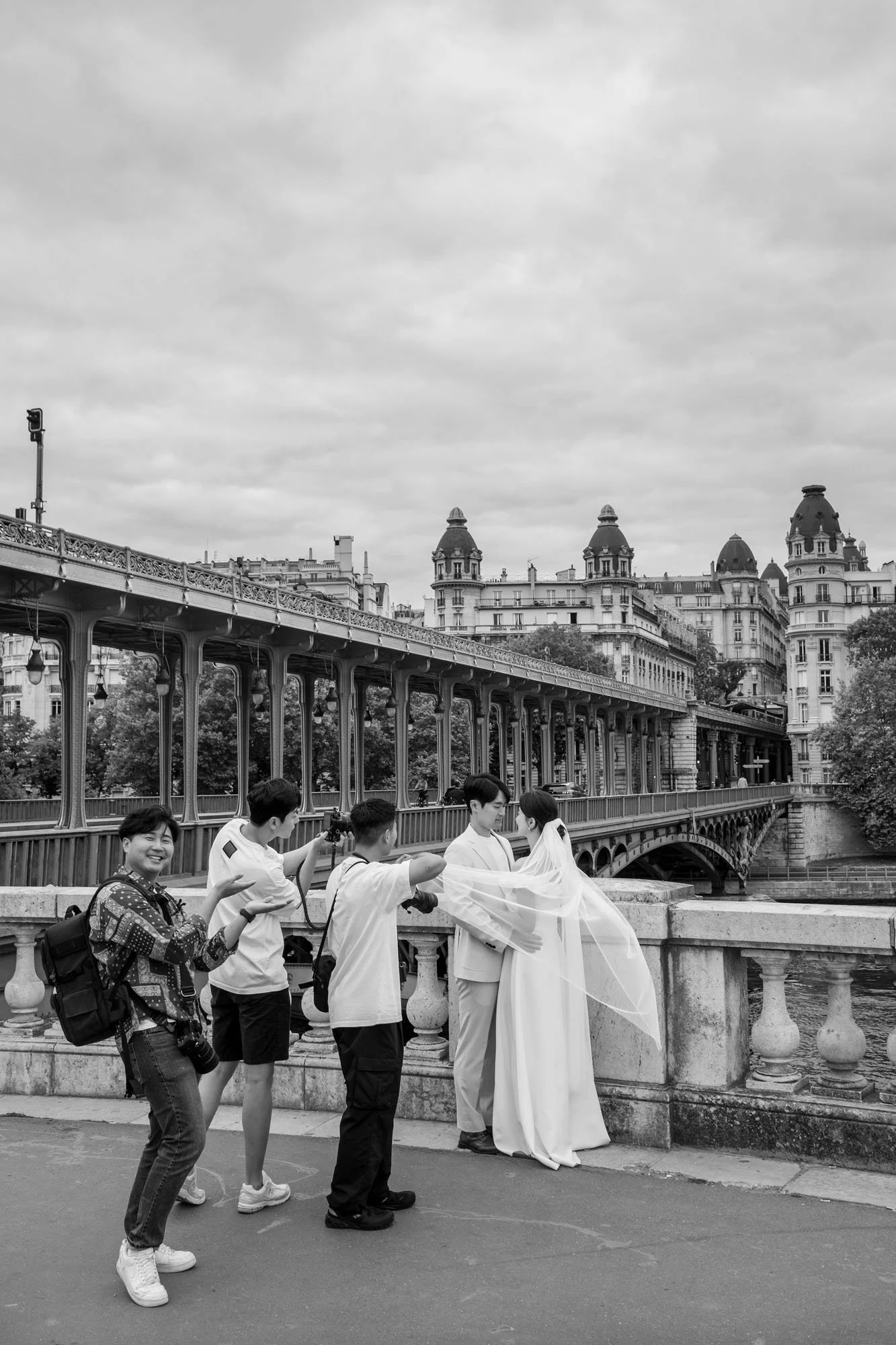  Photographer shooting a bride and groom at the balustrade, the metro viaduct behind, Pont de Bir-Hakeim, Paris. Street photograph by Chris Perona. 