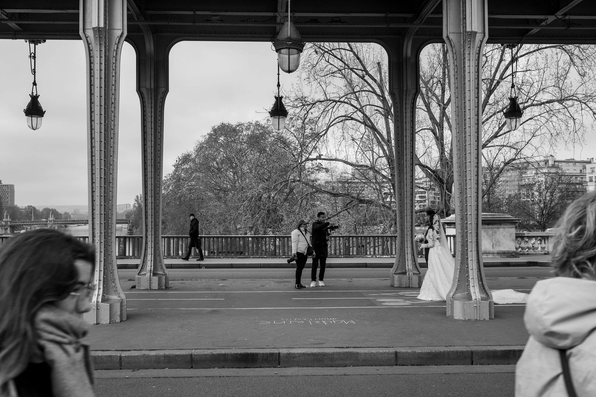  Bride and groom framed between the iron columns of the colonnade, Pont de Bir-Hakeim, Paris. Street photograph by Chris Perona. 
