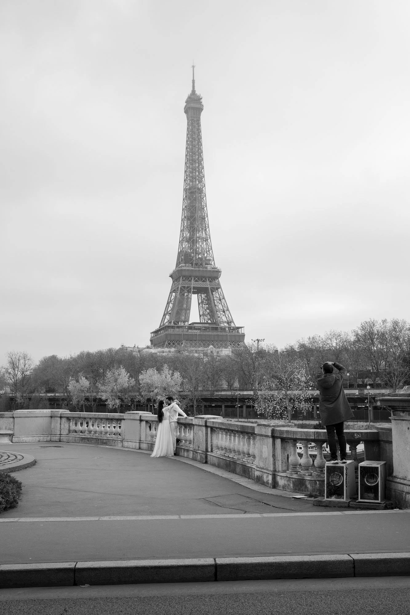  Bride at the balustrade with her photographer, the Eiffel Tower behind, Pont de Bir-Hakeim, Paris. Street photograph by Chris Perona. 