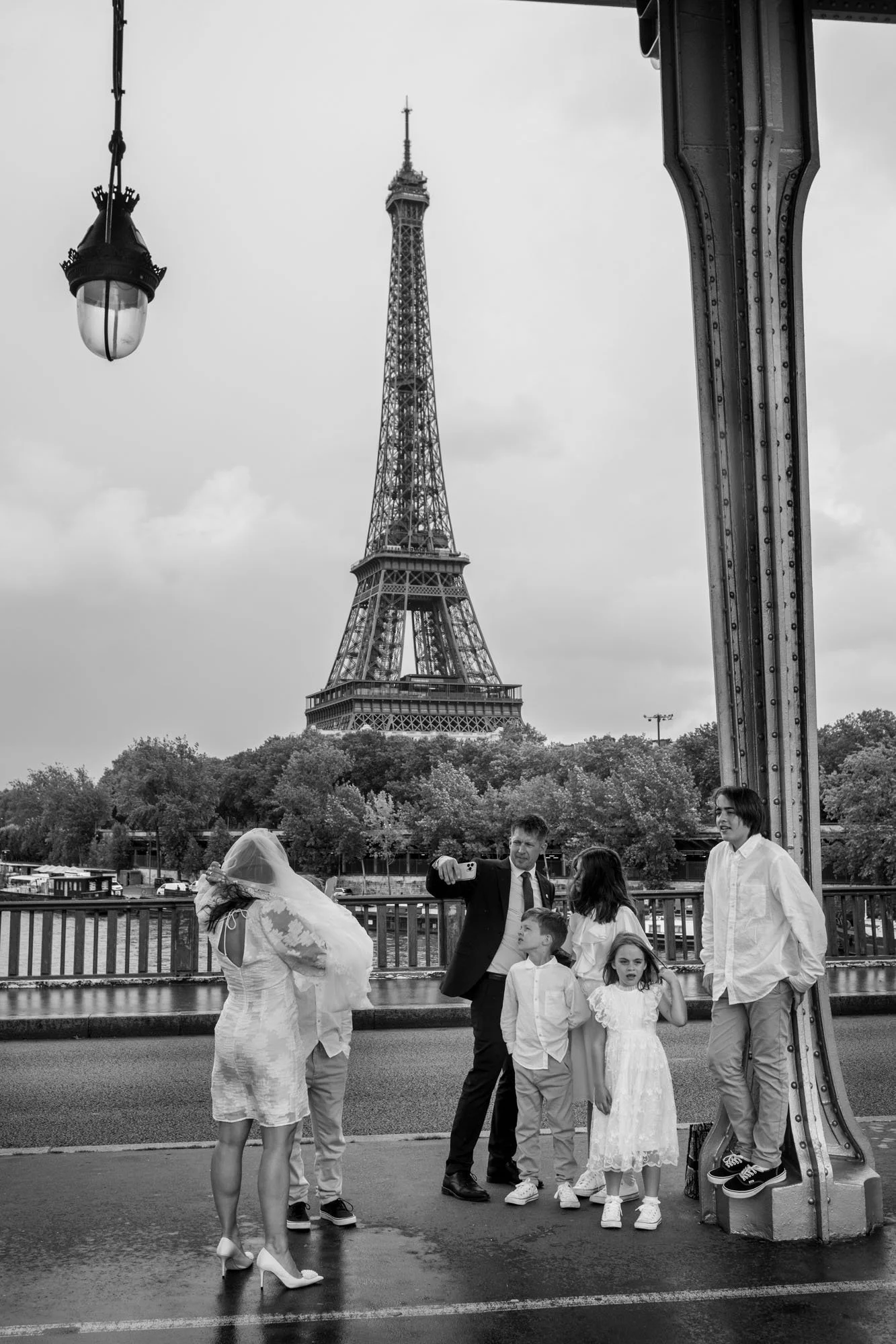  Family dressed in white posing beneath a street lamp, the Eiffel Tower behind, Pont de Bir-Hakeim, Paris. Street photograph by Chris Perona. 