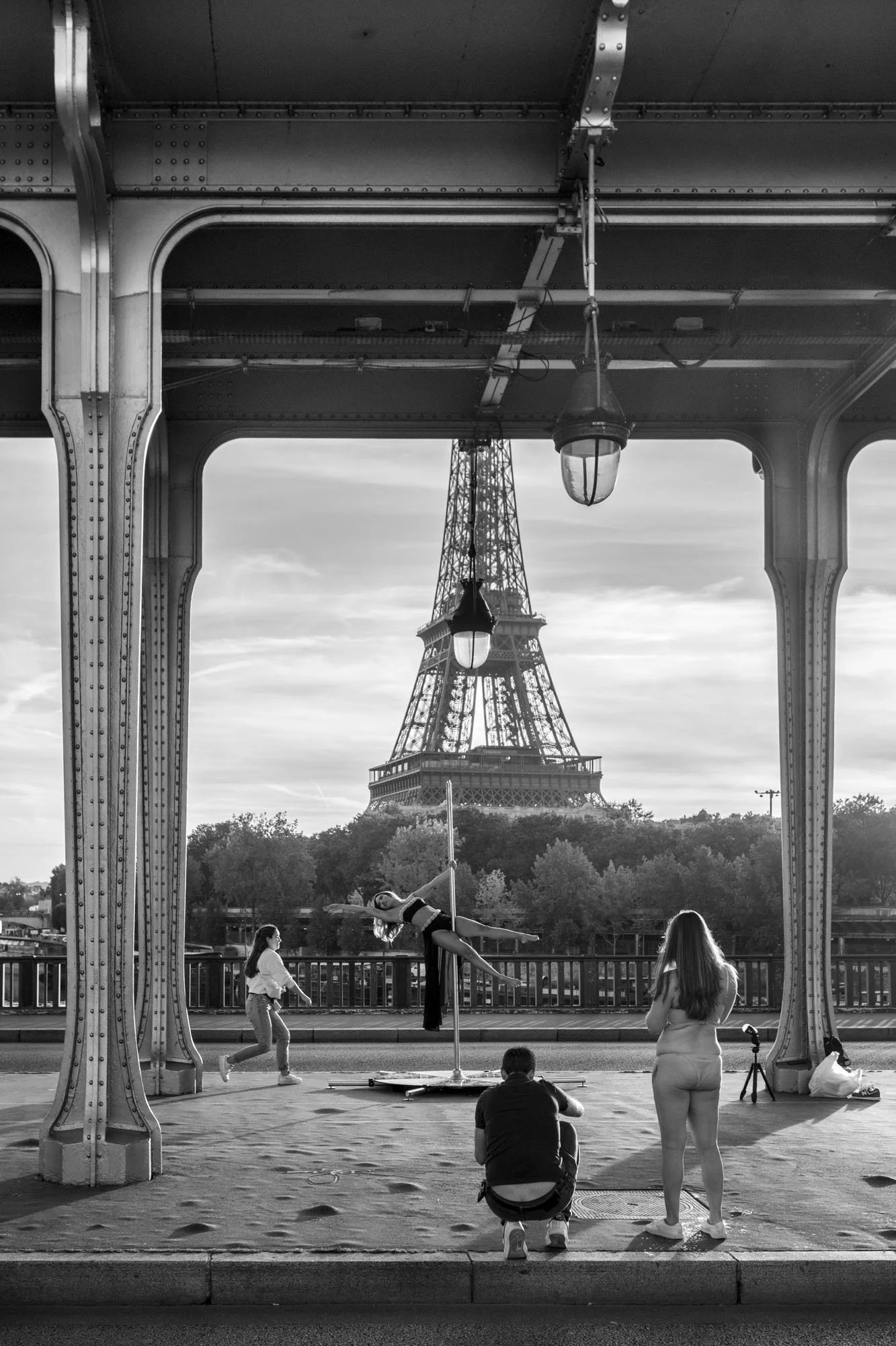  Dancer leaping between the iron columns that frame the Eiffel Tower, Pont de Bir-Hakeim, Paris. Street photograph by Chris Perona. 