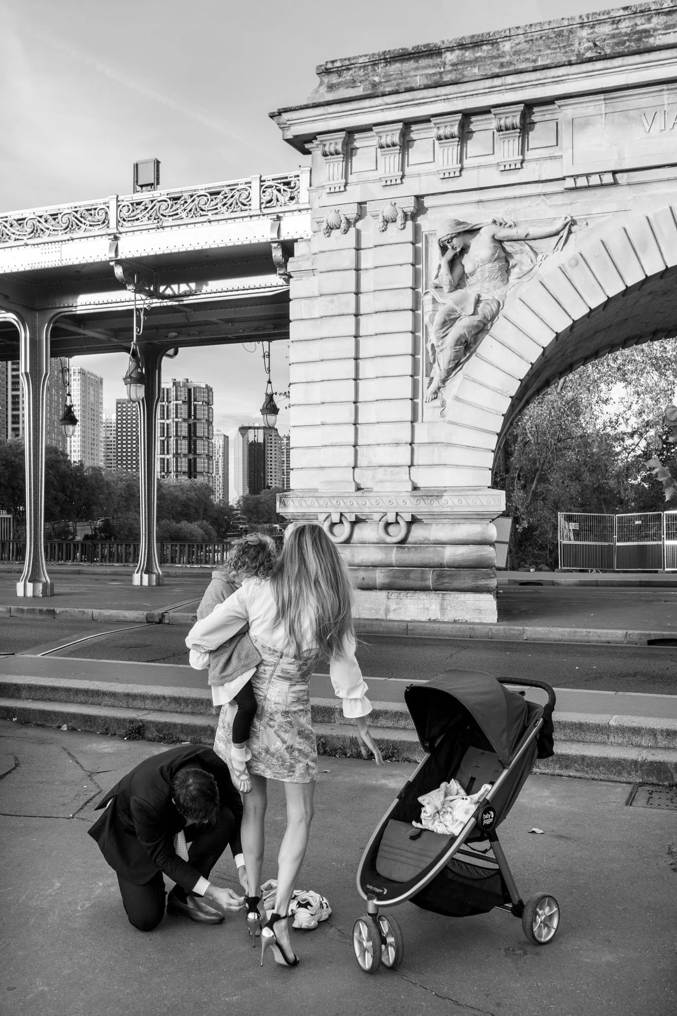  Woman holding a child beside a pushchair beneath the stone arch, Pont de Bir-Hakeim, Paris. Street photograph by Chris Perona. 