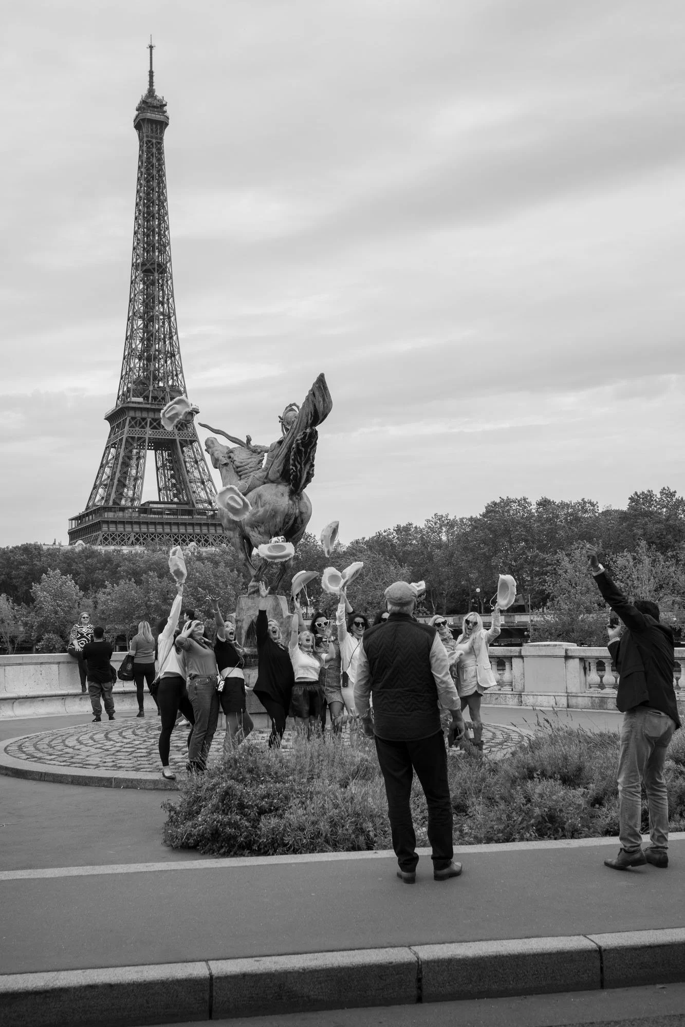  Group of visitors raising their arms for a photo before the statue and the Eiffel Tower, Pont de Bir-Hakeim, Paris. Street photograph by Chris Perona. 