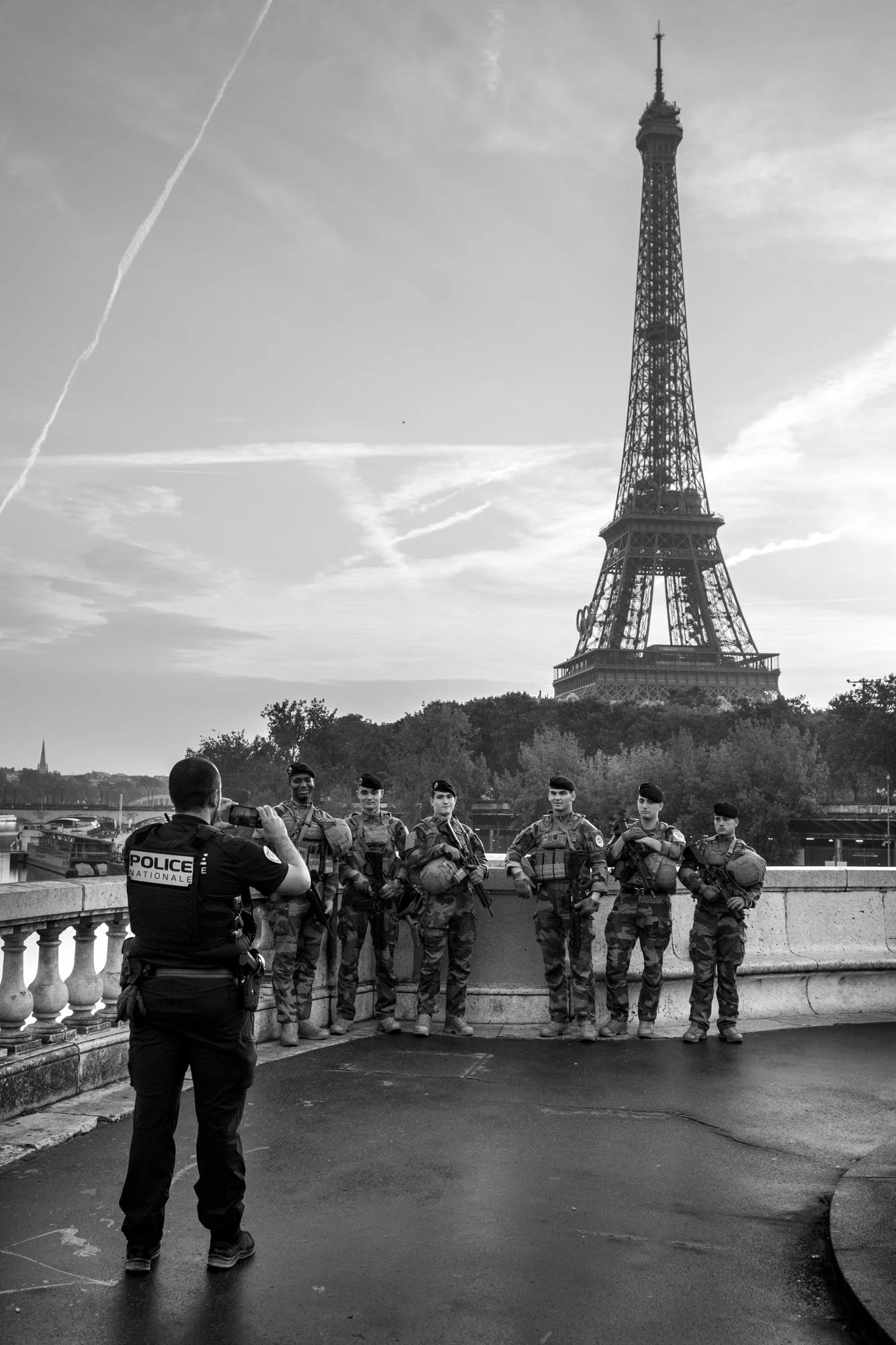  Police officer and soldiers on patrol at the balustrade, the Eiffel Tower behind, Pont de Bir-Hakeim, Paris. Street photograph by Chris Perona. 