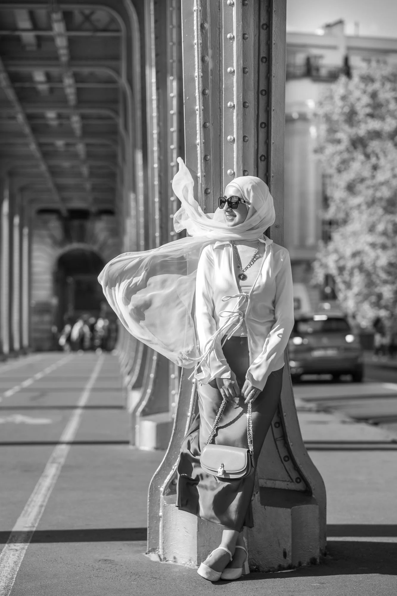  Woman in a white headscarf posing with fabric flowing in the wind beneath the viaduct, Pont de Bir-Hakeim, Paris. Street photograph by Chris Perona. 