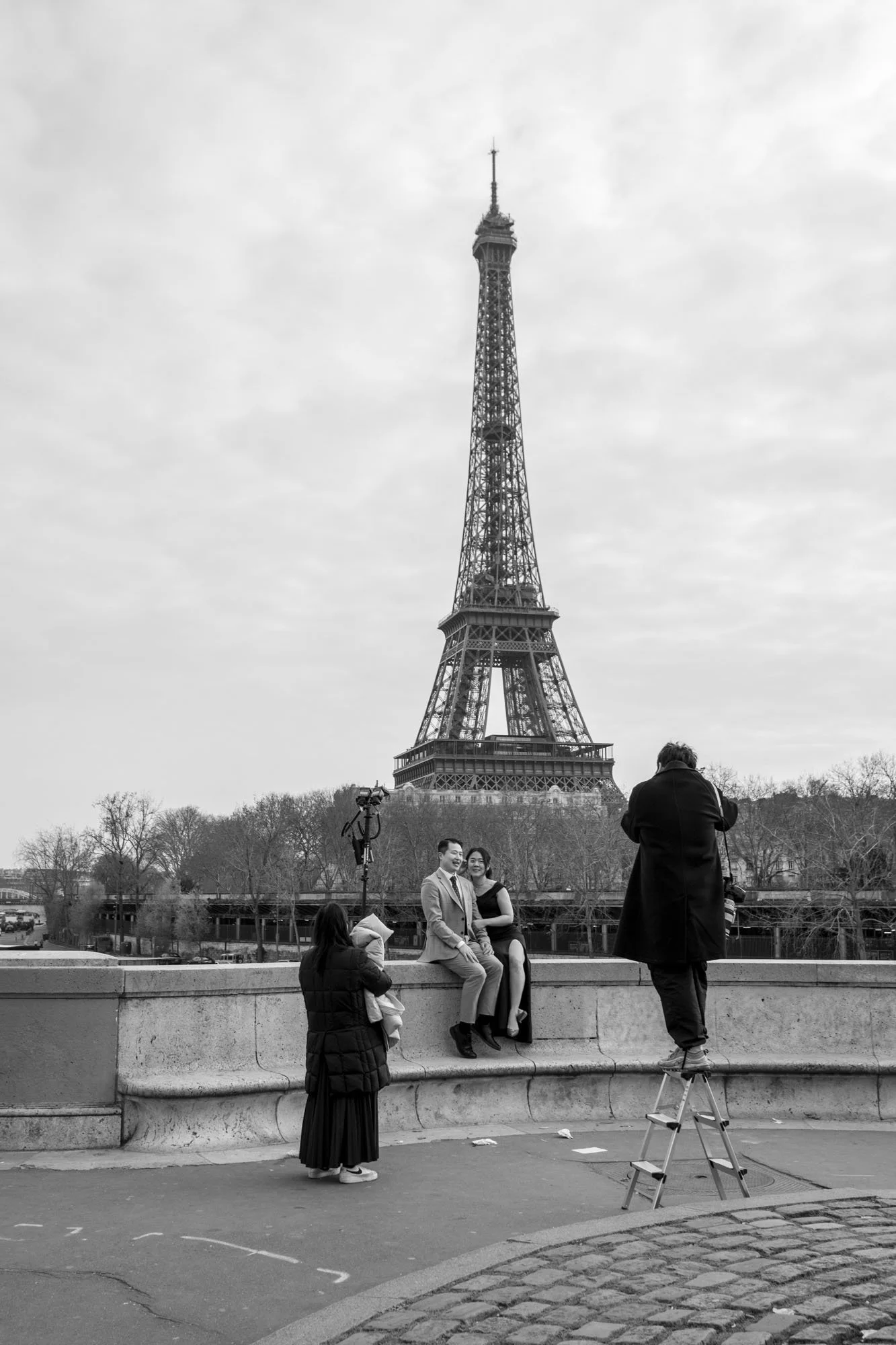  Photographer on a stepladder shooting a couple on the parapet before the Eiffel Tower, Pont de Bir-Hakeim, Paris. Street photograph by Chris Perona. 