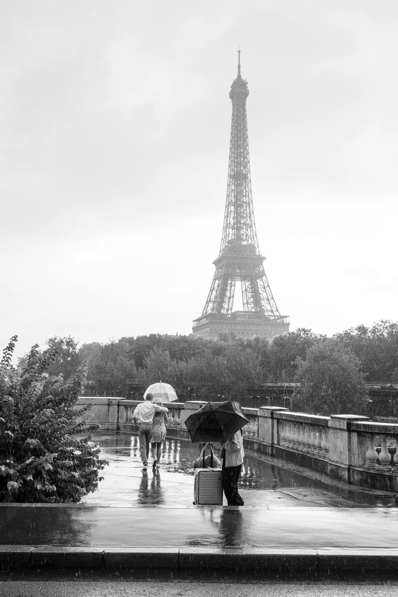  Visitors with umbrellas on the rain-soaked bridge, the Eiffel Tower in mist, Pont de Bir-Hakeim, Paris. Street photograph by Chris Perona. 