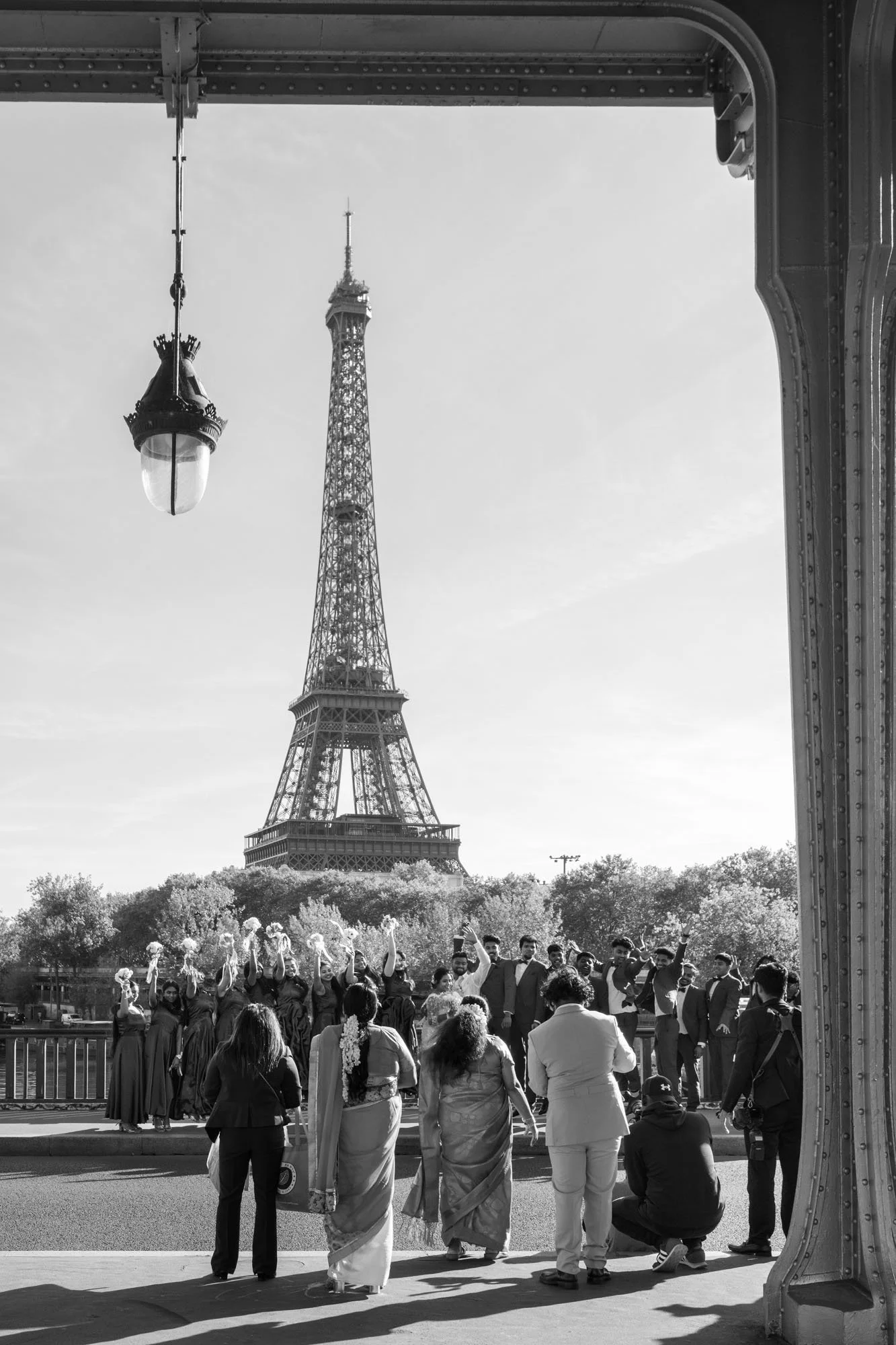  Group in traditional dress being photographed beneath the colonnade, the Eiffel Tower framed, Pont de Bir-Hakeim, Paris. Street photograph by Chris Perona. 