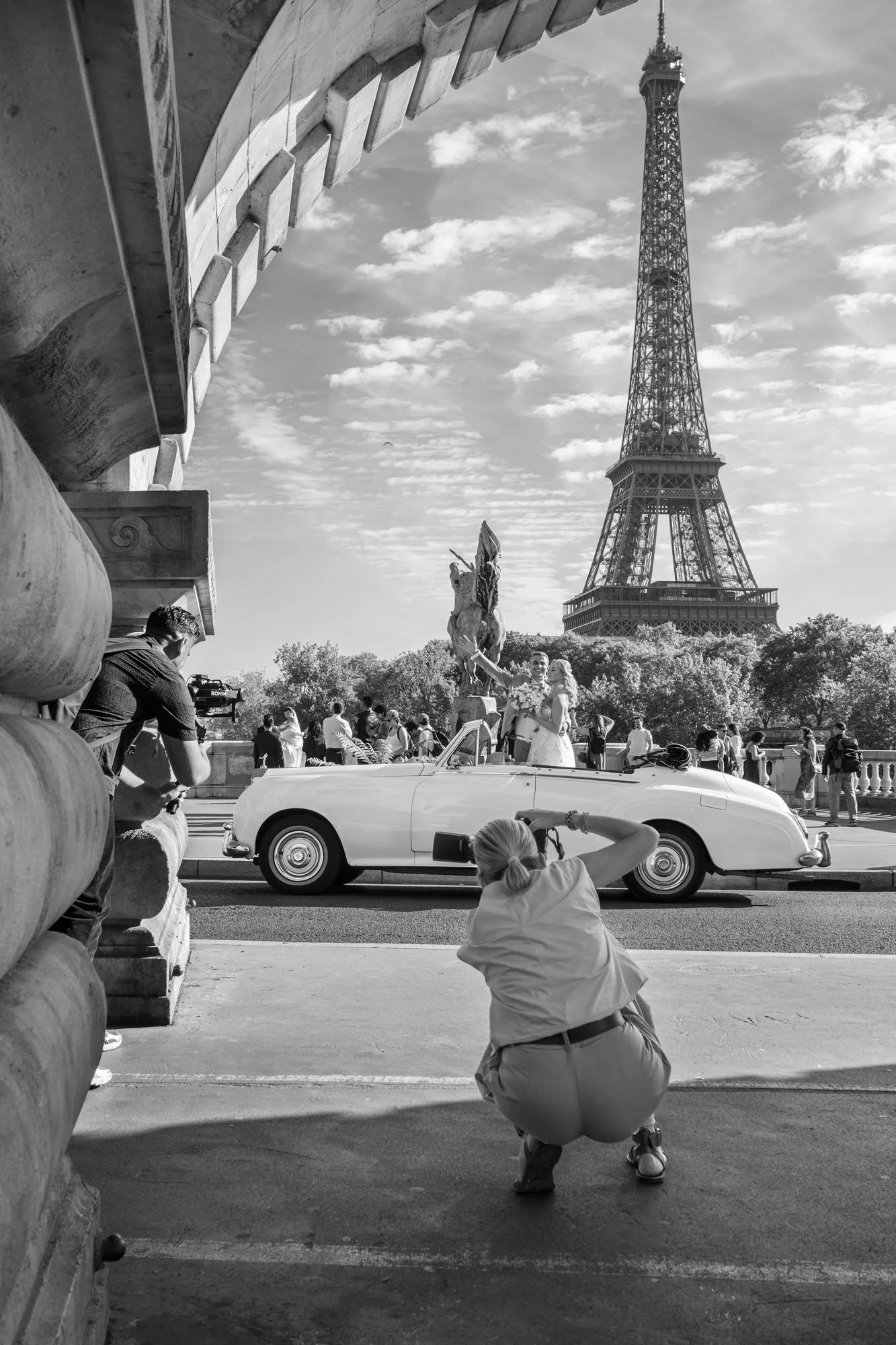  Photographer crouching to shoot a vintage convertible before the Eiffel Tower, Pont de Bir-Hakeim, Paris. Street photograph by Chris Perona. 