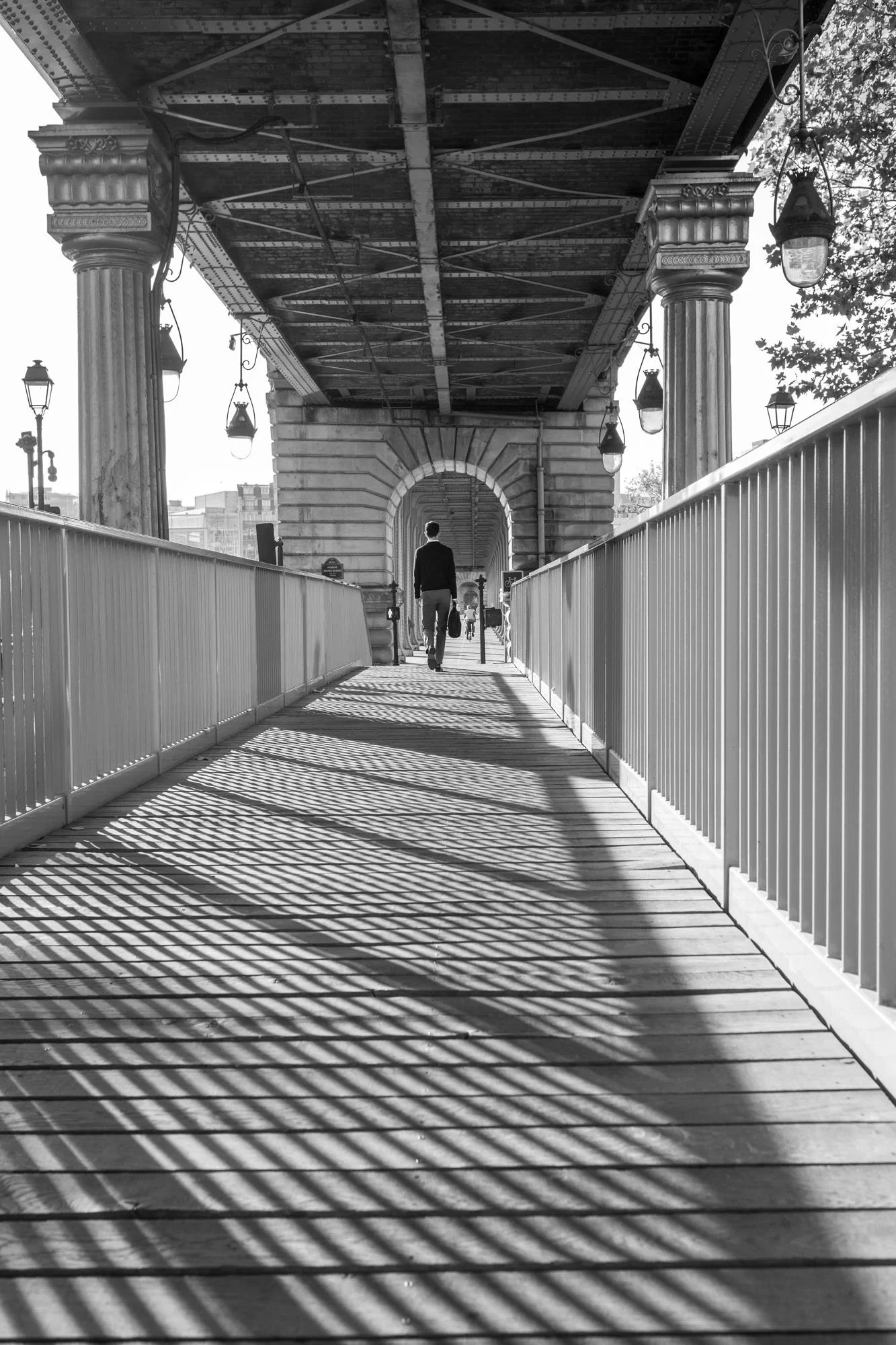  Striped shadows on the walkway beneath the metro deck as a figure walks away, Pont de Bir-Hakeim, Paris. Architecture photograph by Chris Perona. 