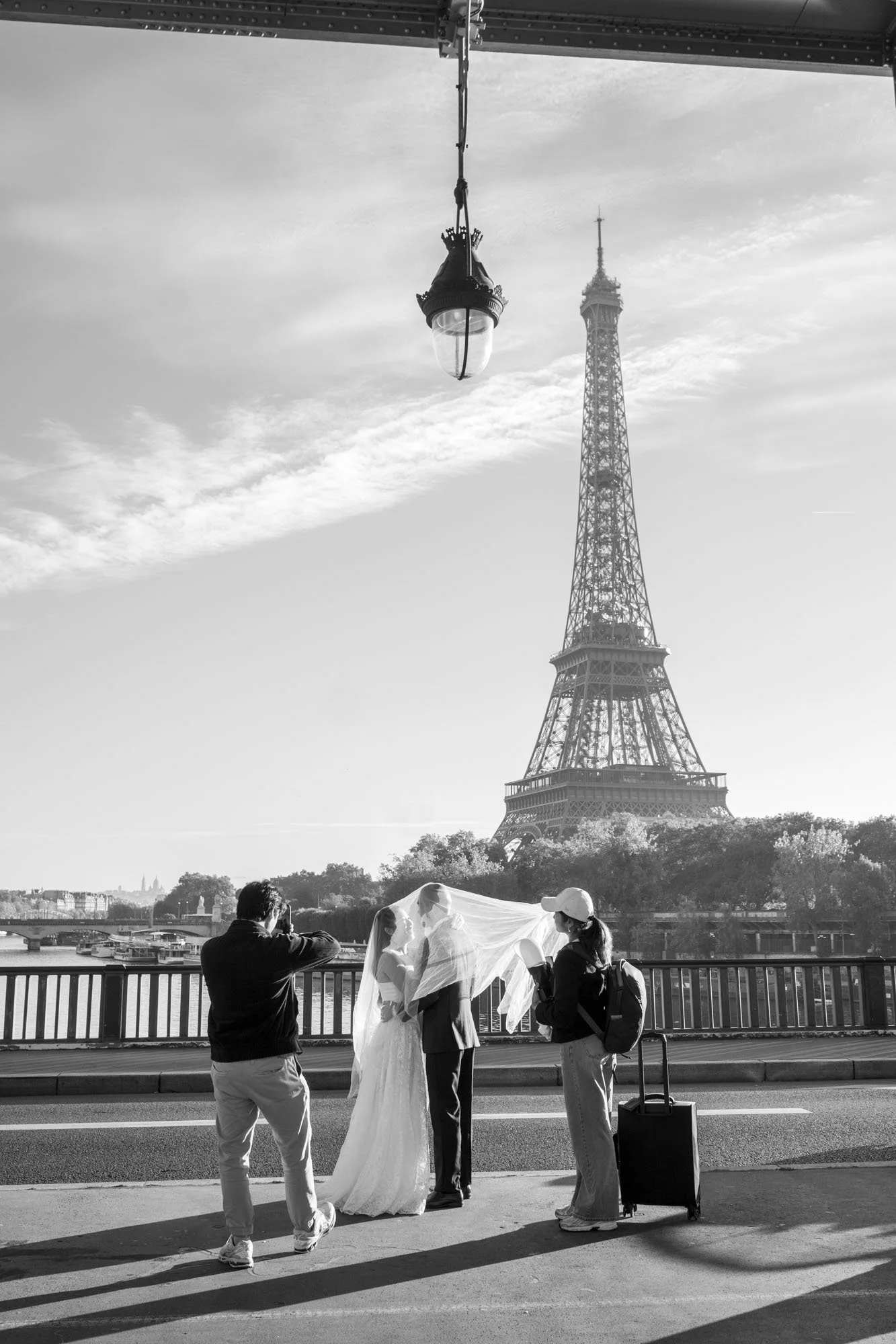  Wedding photographer and assistant arranging a bride's veil before the Eiffel Tower, Pont de Bir-Hakeim, Paris. Street photograph by Chris Perona. 