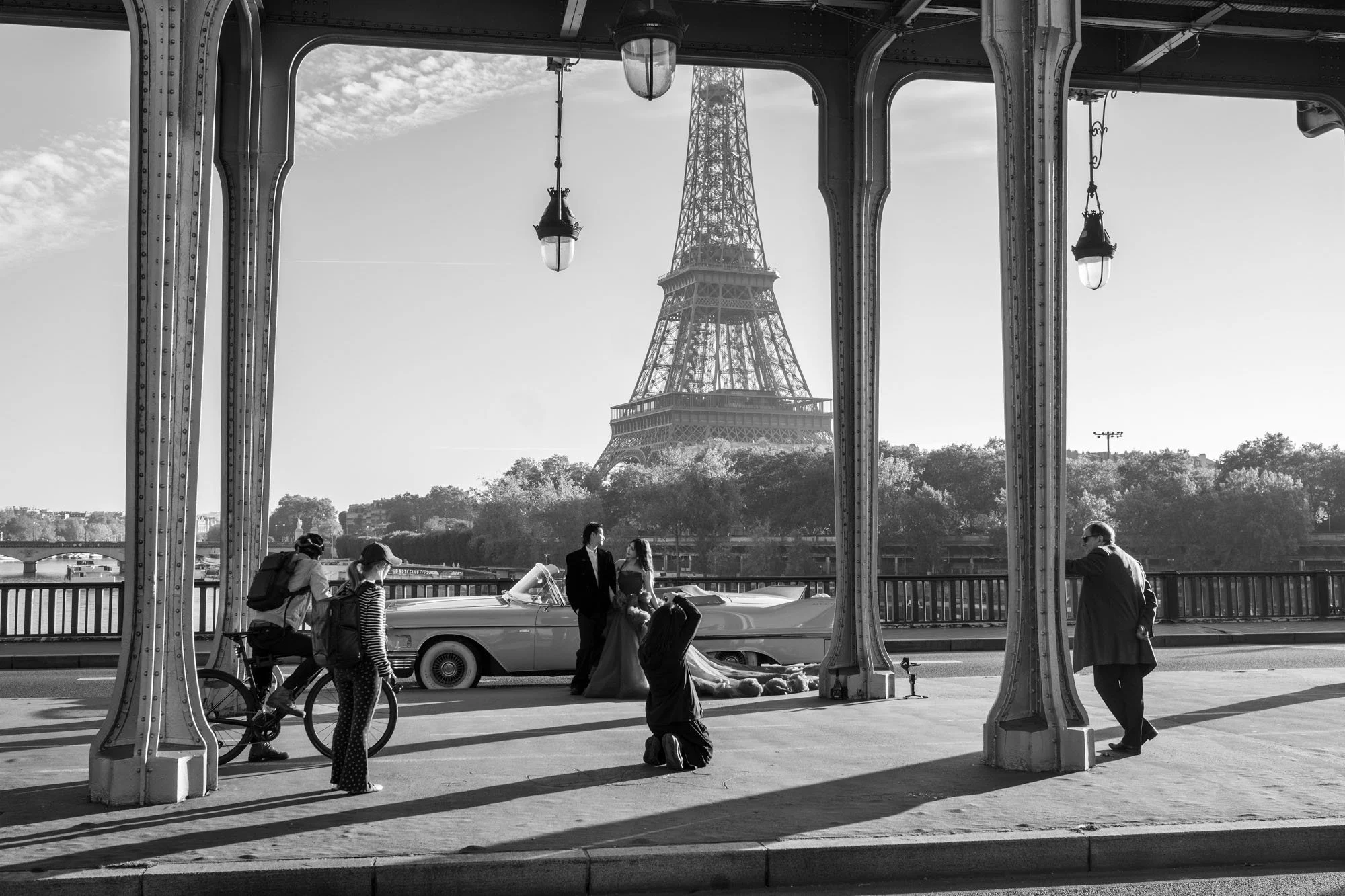  Wedding party and a vintage car beneath the colonnade, the Eiffel Tower framed, Pont de Bir-Hakeim, Paris. Street photograph by Chris Perona. 