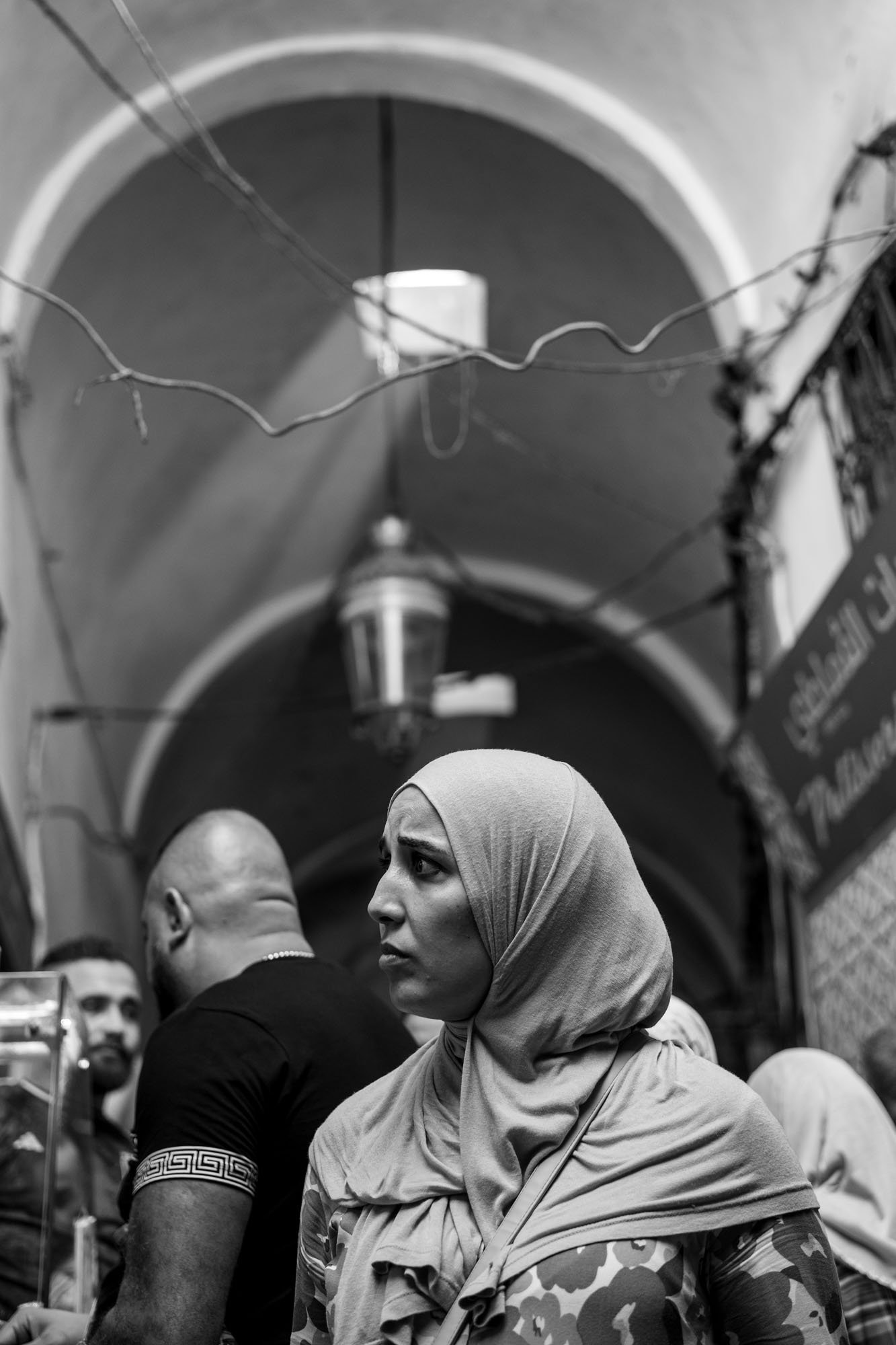  Woman in a headscarf in a crowded vaulted souk, light falling from above, medina of Tunis. Black-and-white street photograph by Chris Perona. 