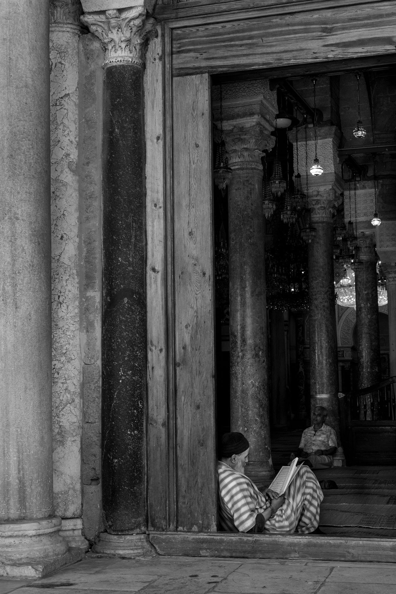  Man reading in the doorway of a mosque, its columned prayer hall behind, medina of Tunis. Black-and-white street photograph by Chris Perona. 
